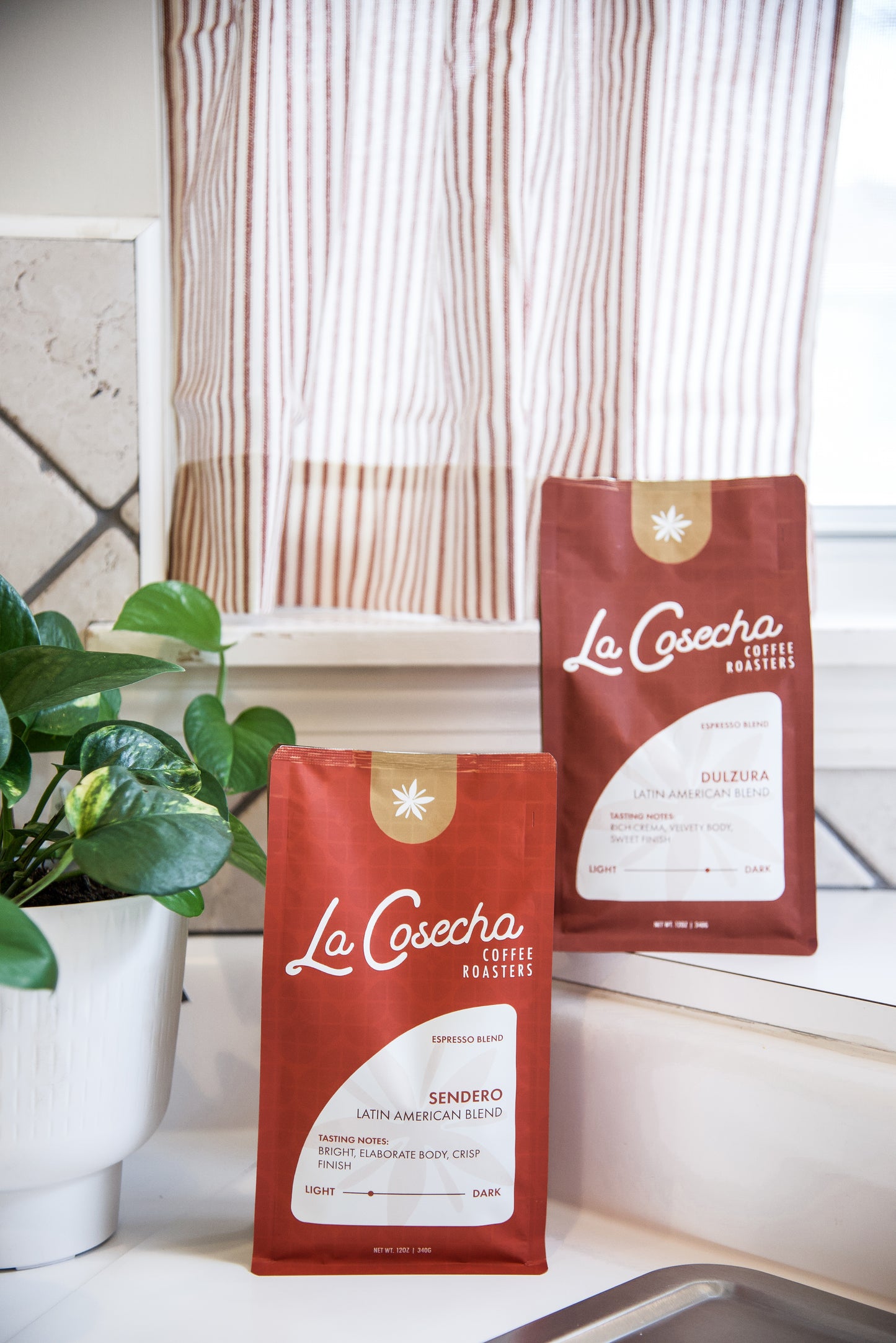 Two red 'La Cosecha' coffee bags on a kitchen counter with a plant in the background.