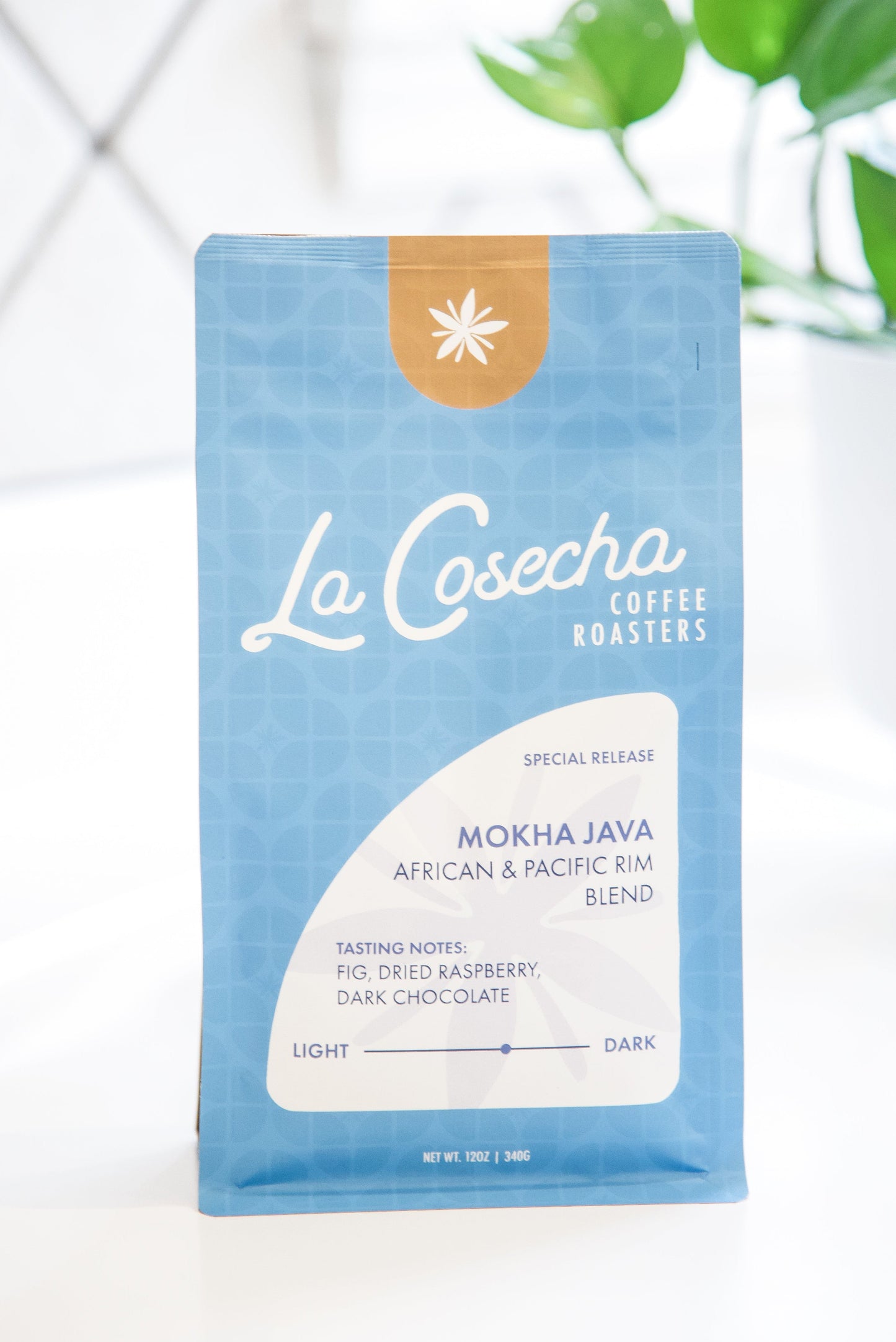 La Cosecha Coffee Roasters bag on a white surface with a plant in the background