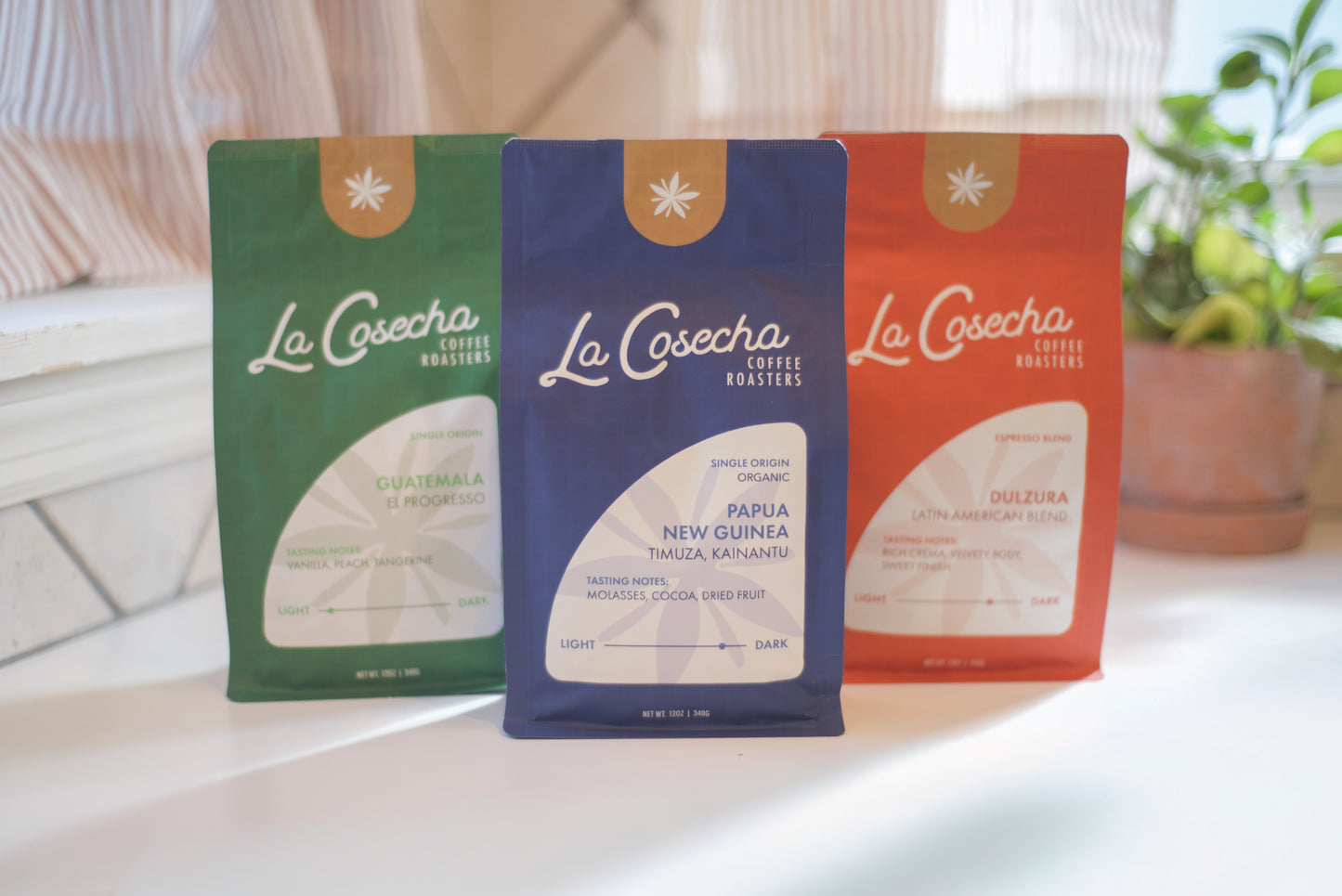 Three La Cosecha coffee packages on a table with a blurred background