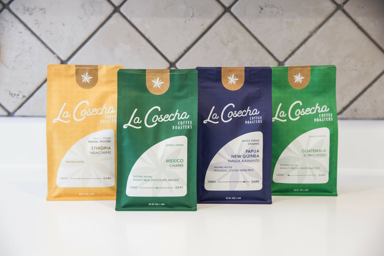 Four 'La Cosecha' coffee bags on a white surface with a tiled wall background