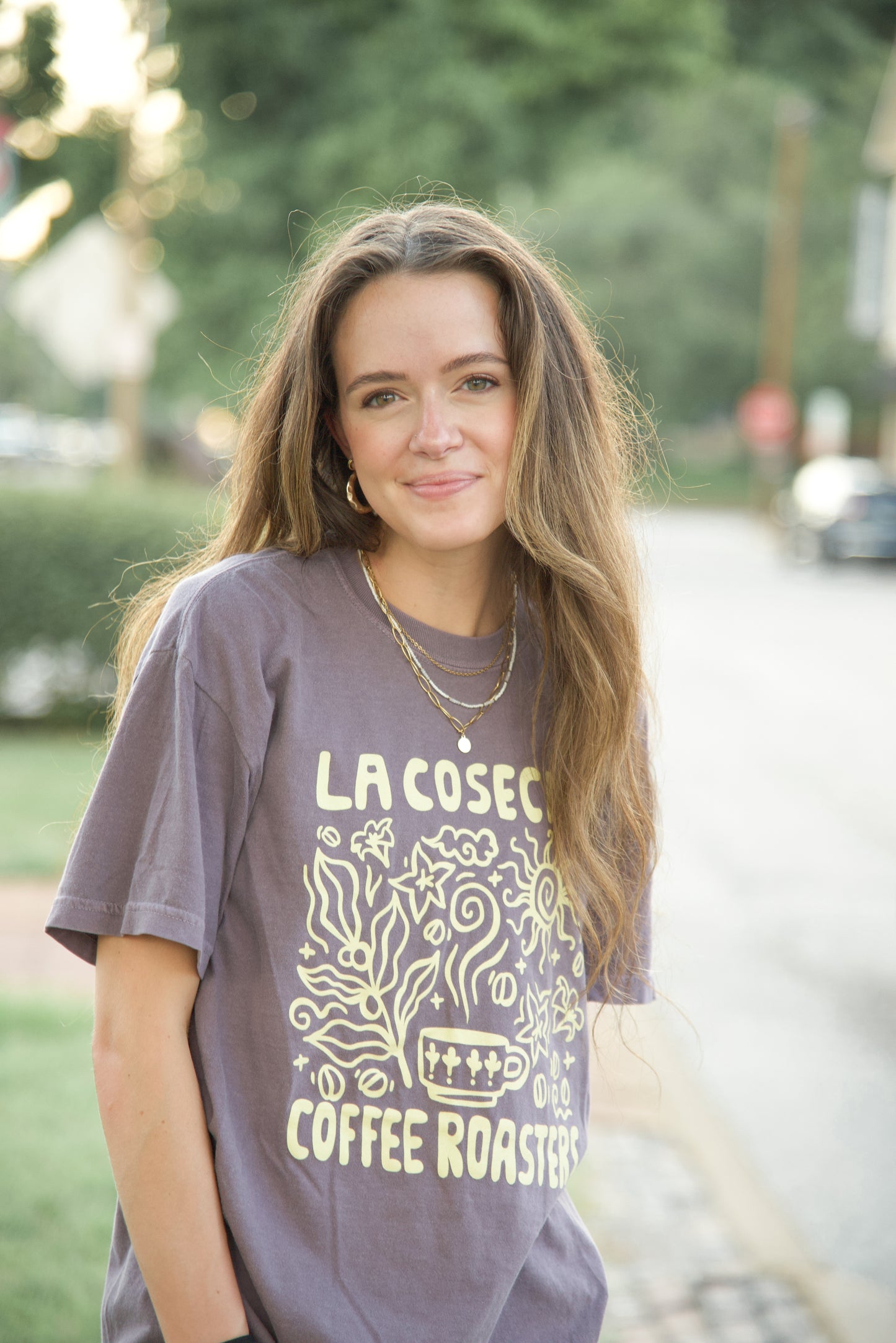 Woman wearing a 'La Coseca Coffee Roasters' t-shirt outdoors.