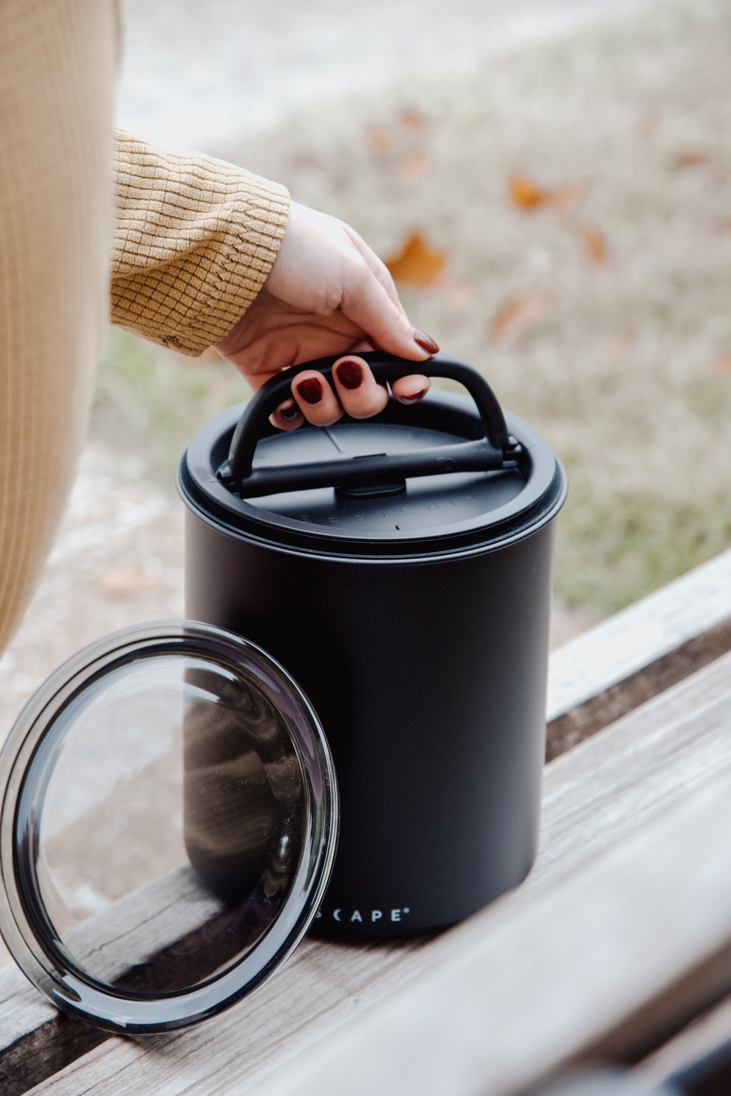 Person holding a black Airscape kilo with a transparent lid on a wooden surface.