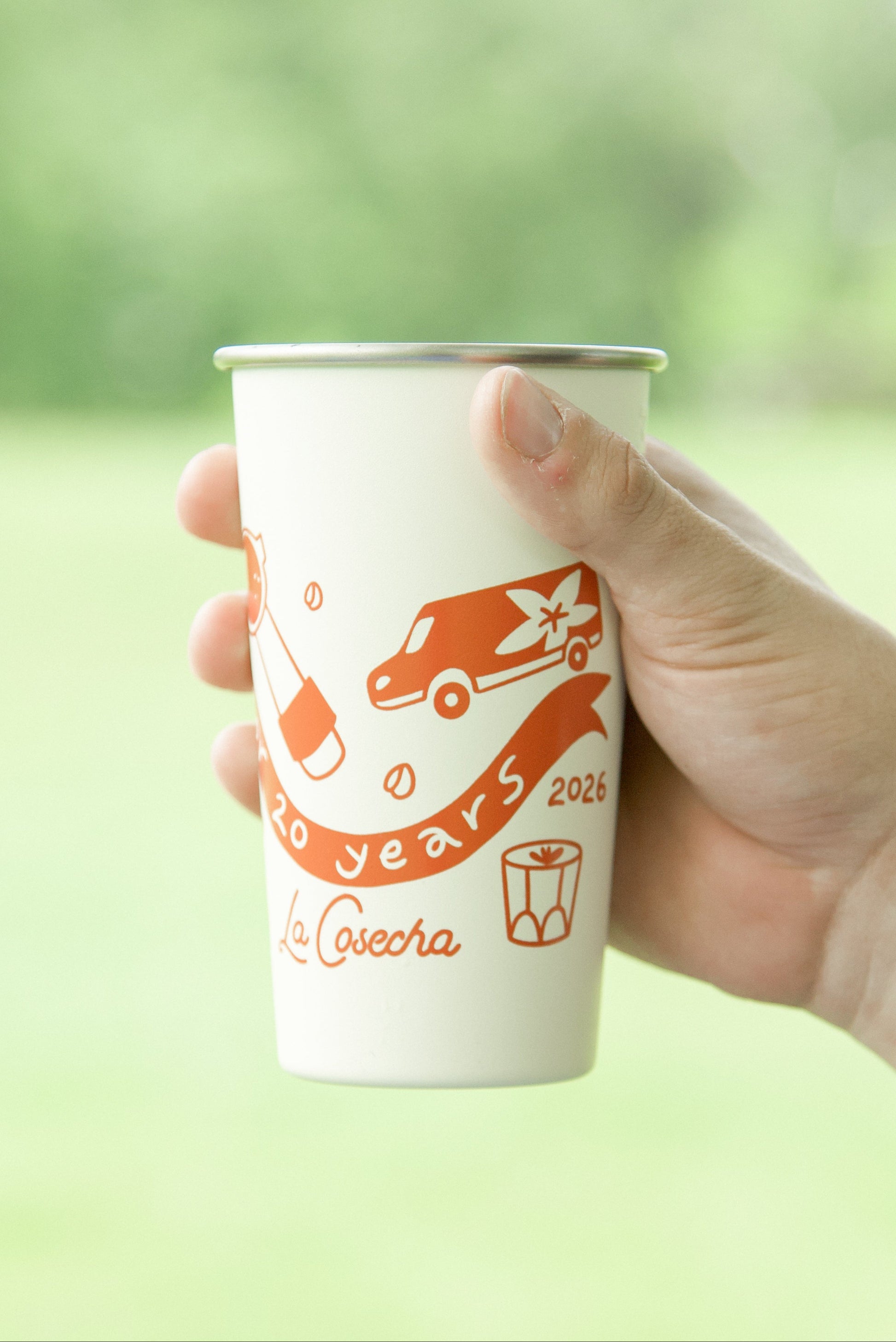 Hand holding a paper cup with a logo against a blurred green outdoor background