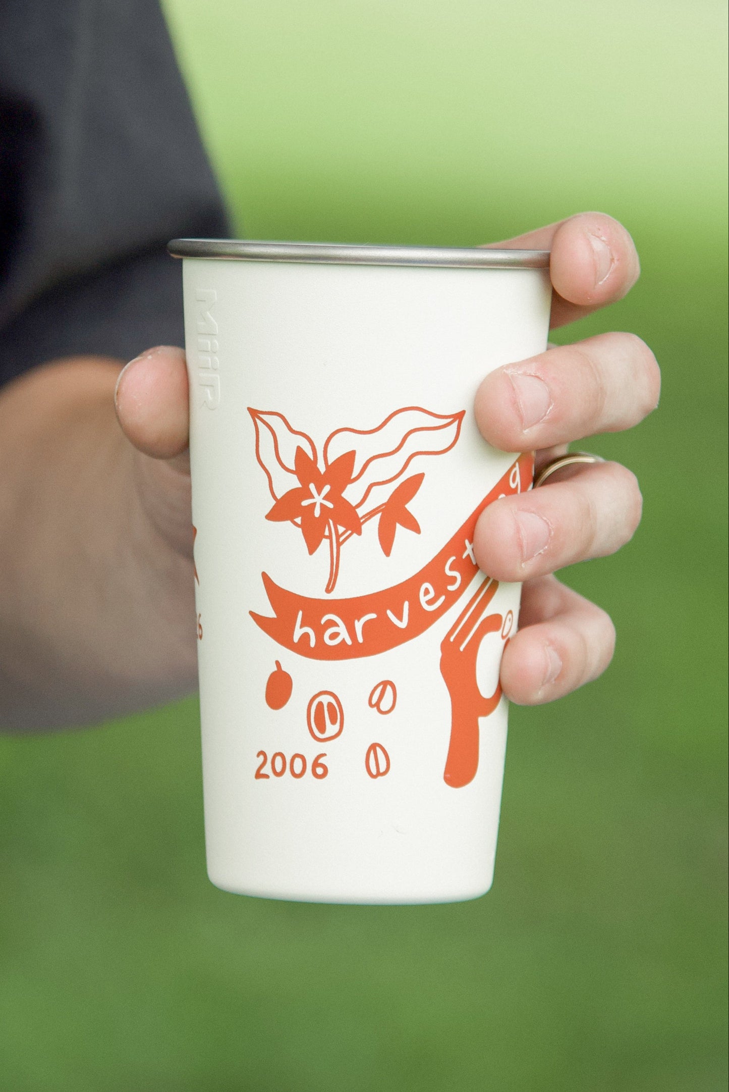 Person holding a white cup with orange design outdoors