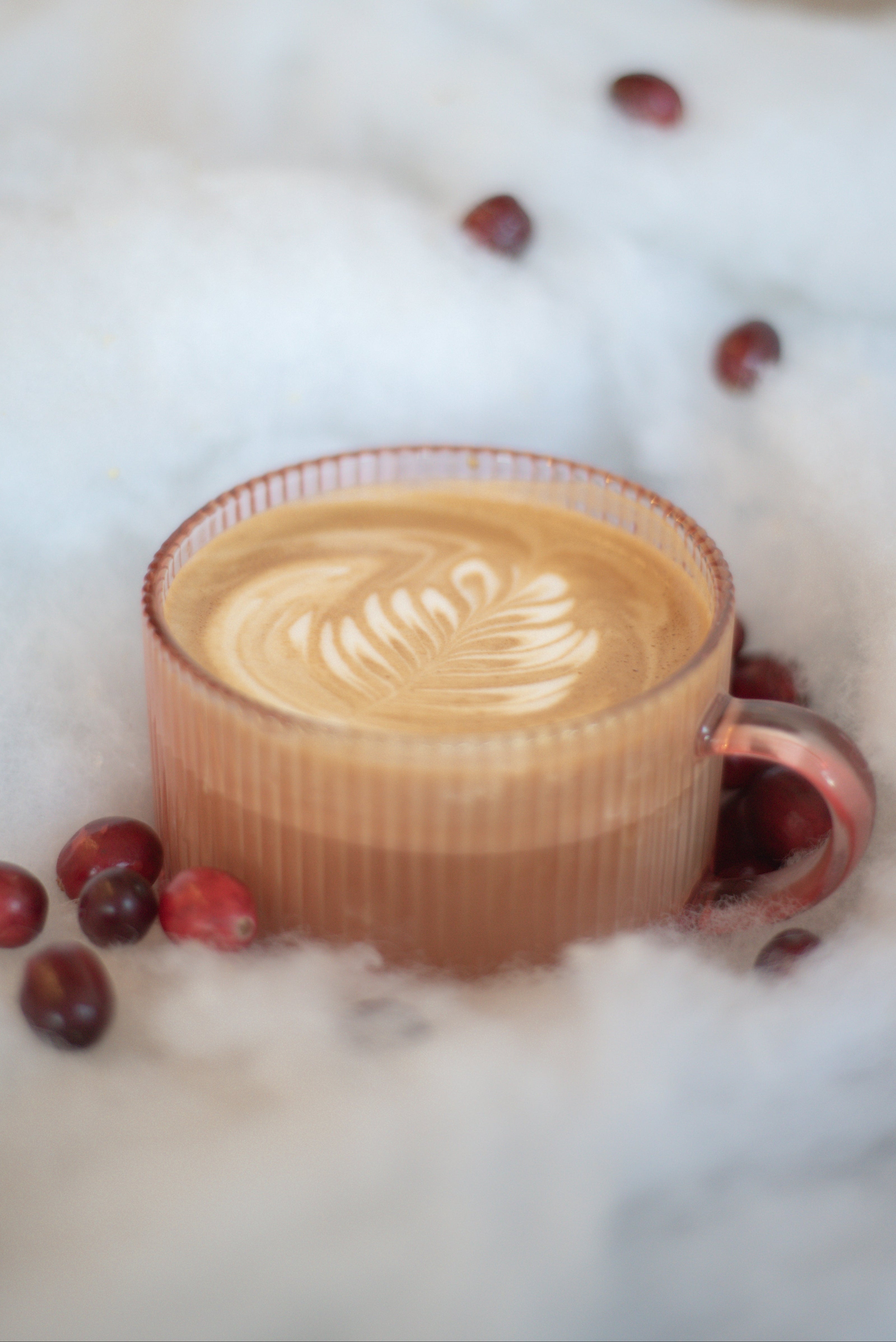 Cappuccino in a glass mug surrounded by red berries on a white background