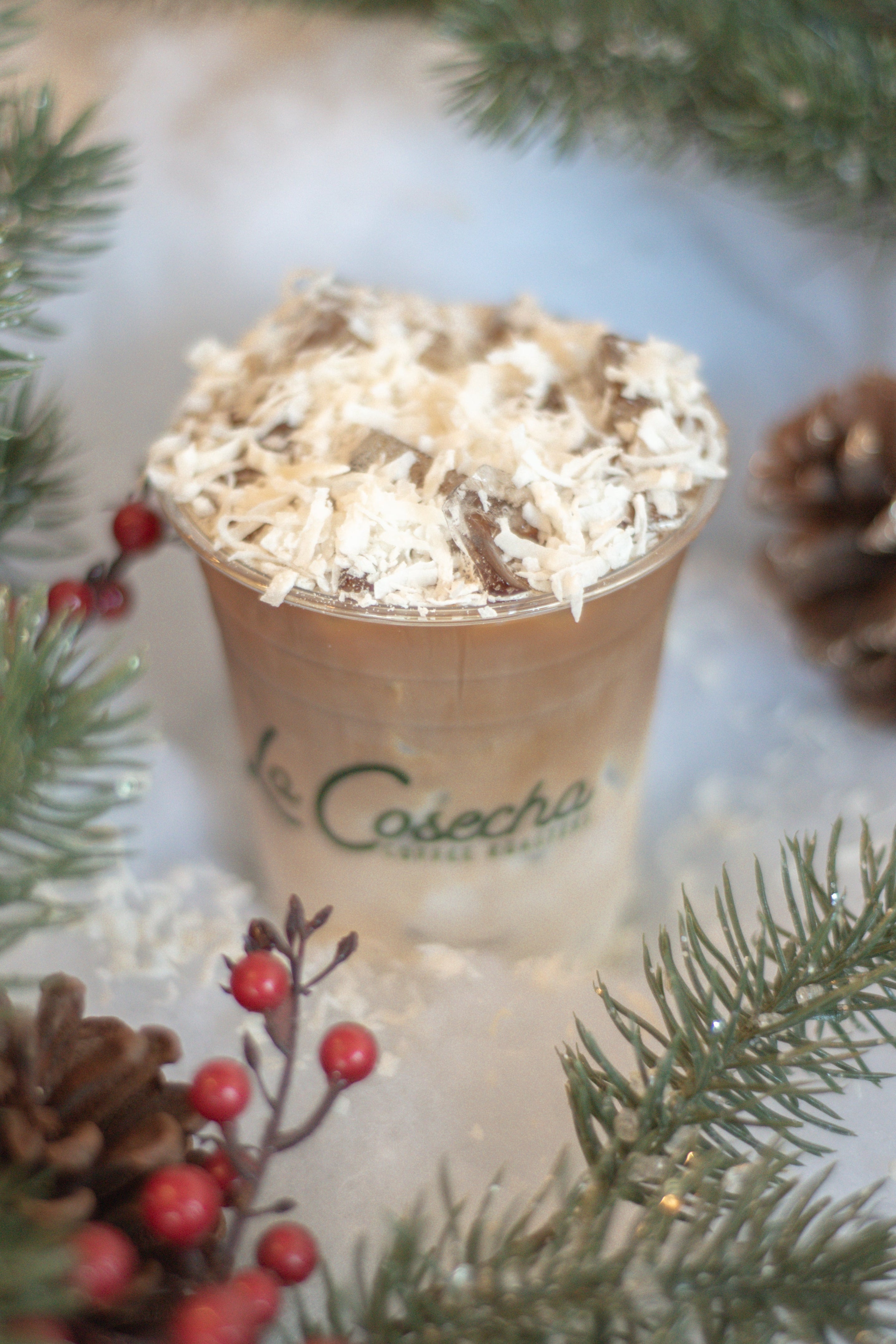 Cup of coffee with whipped cream surrounded by Christmas decorations on a snowy surface