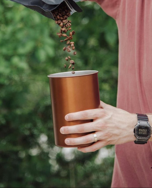 Person pouring coffee beans from a bag into a copper Airscape outside.