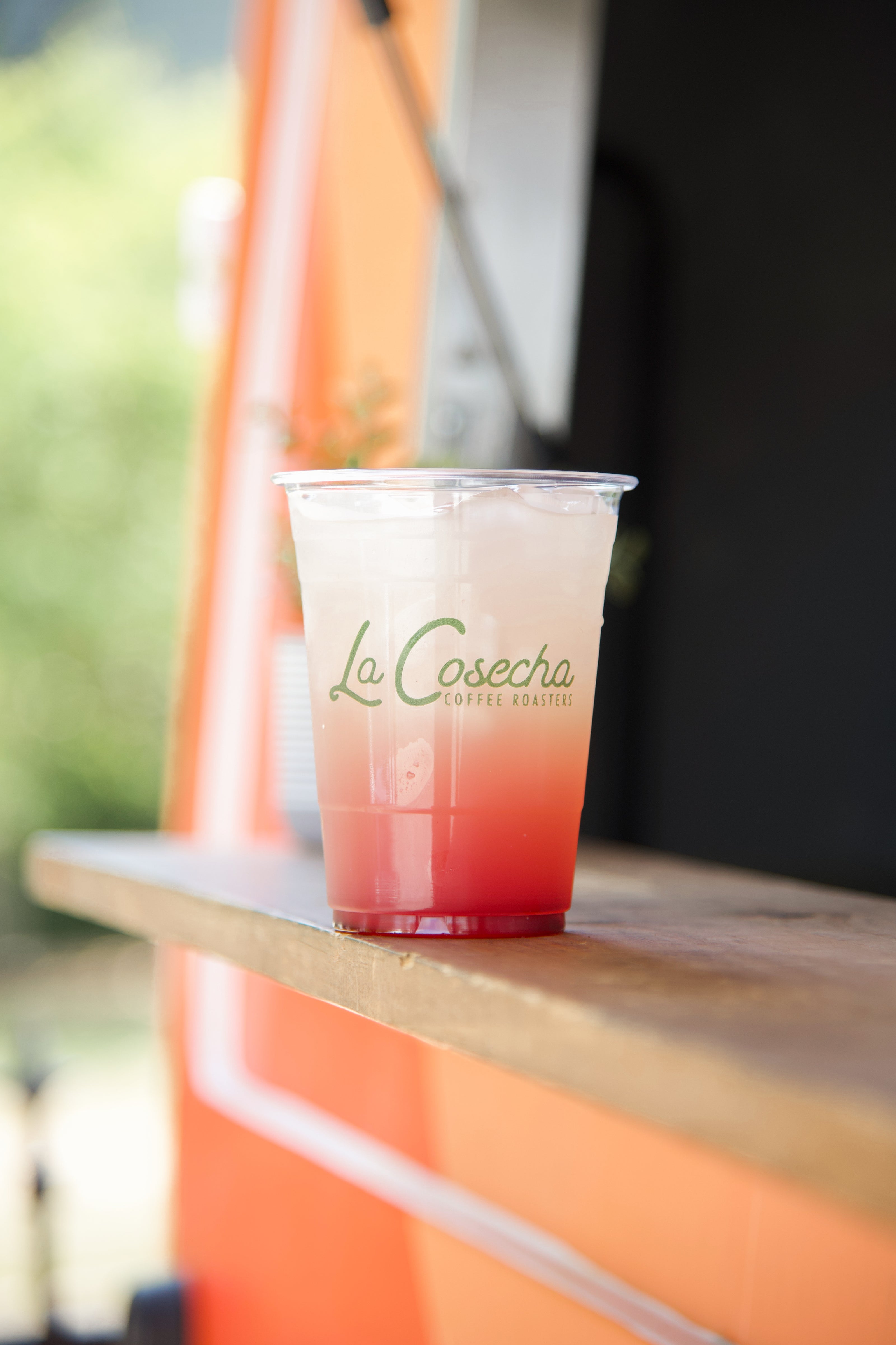 Colorful drink in a clear cup with 'La Cosecha' branding on a wooden surface.
