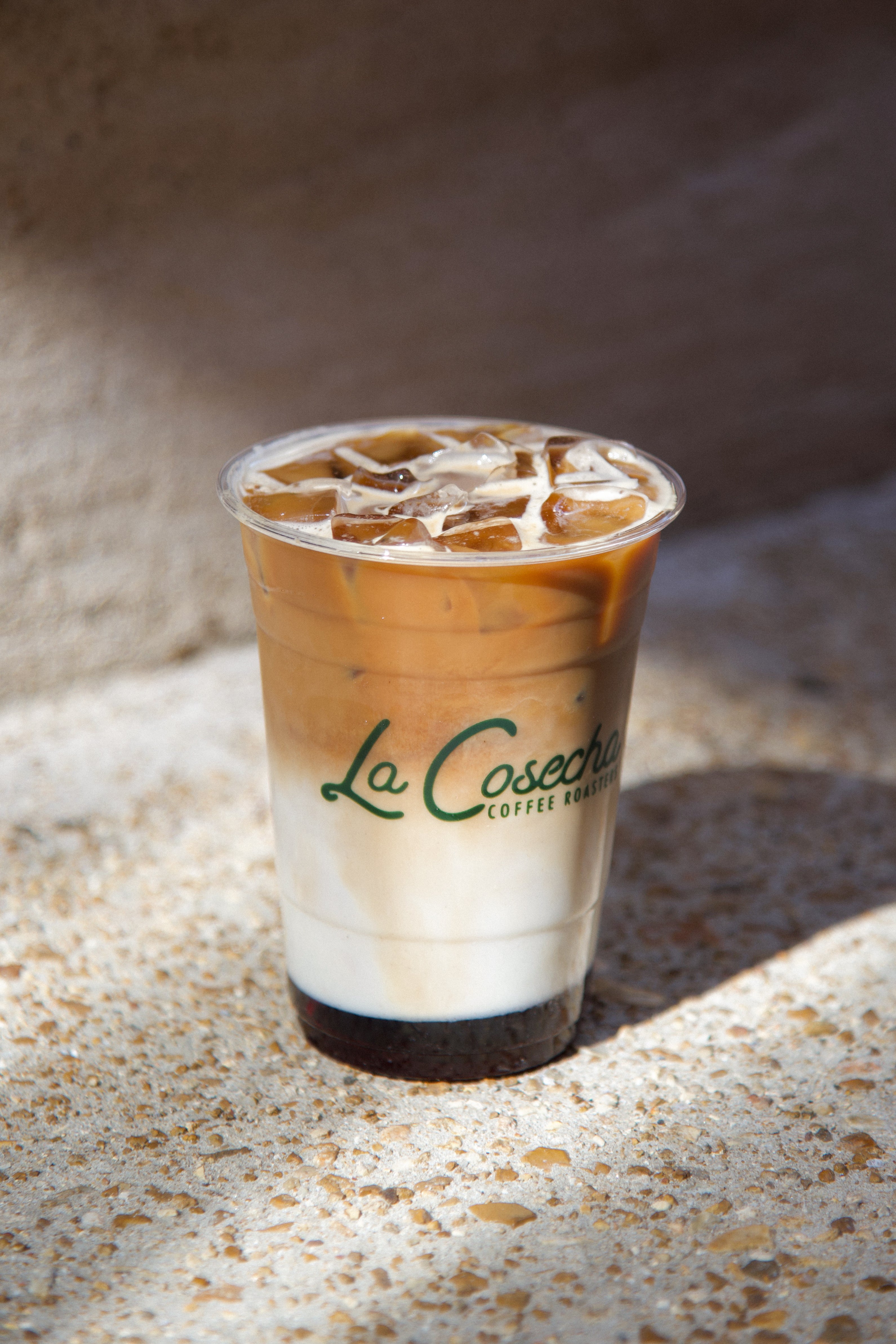 Iced coffee in a clear plastic cup with La Cosecha Coffee branding on a textured surface.
