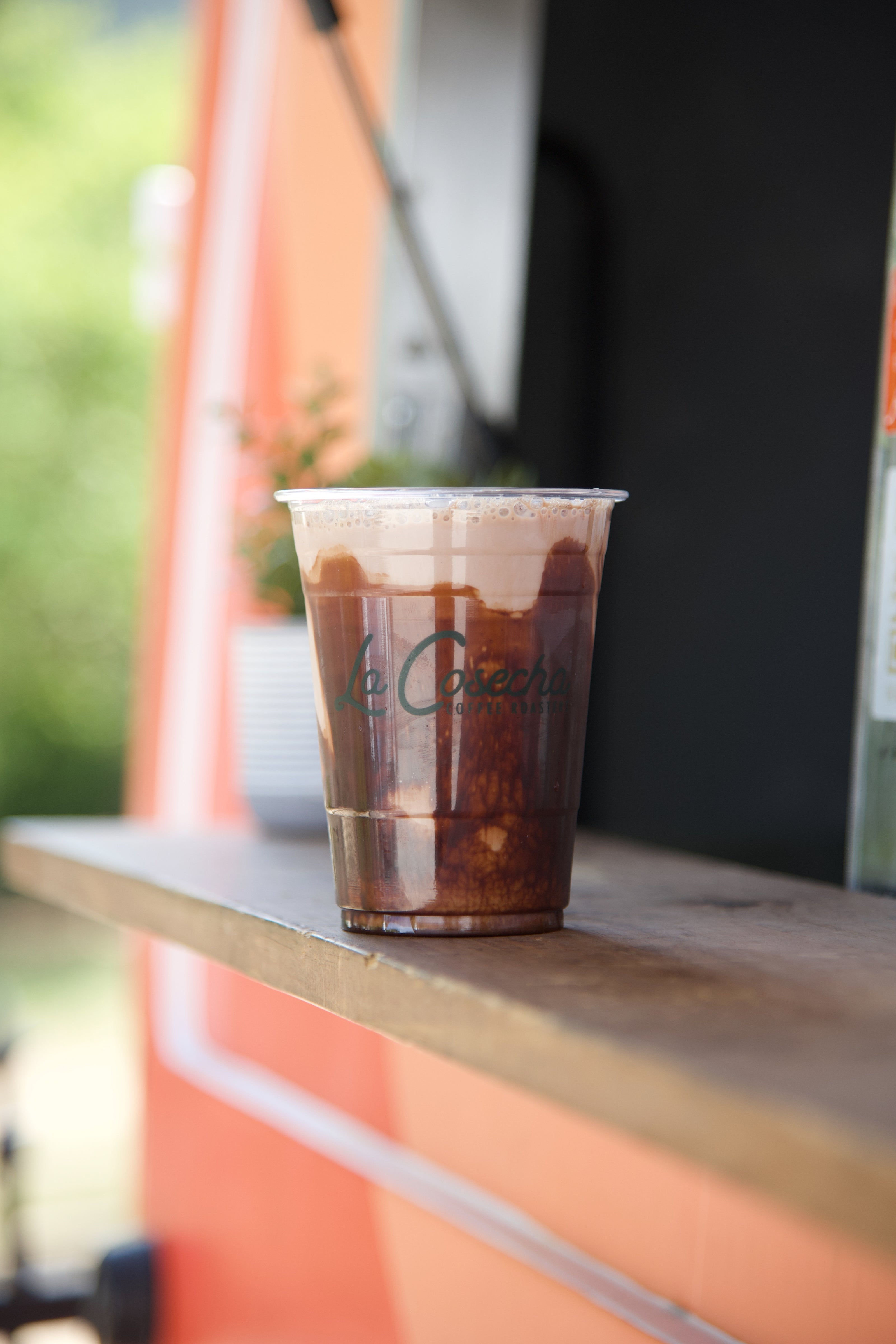 Clear plastic cup with a dark beverage on a wooden surface, blurred background