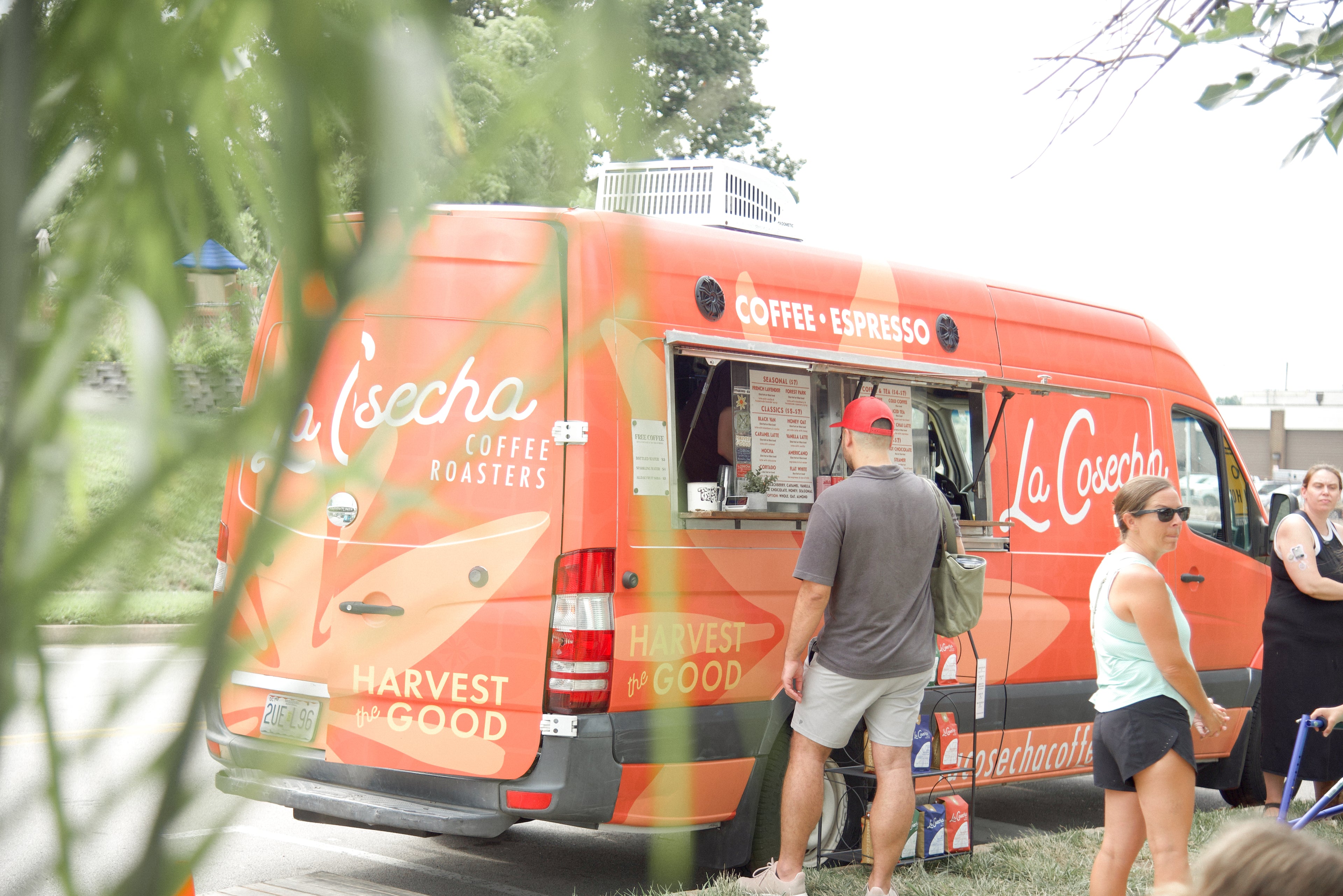 Orange food truck with 'La Cosecha' branding parked outdoors, people interacting around it.