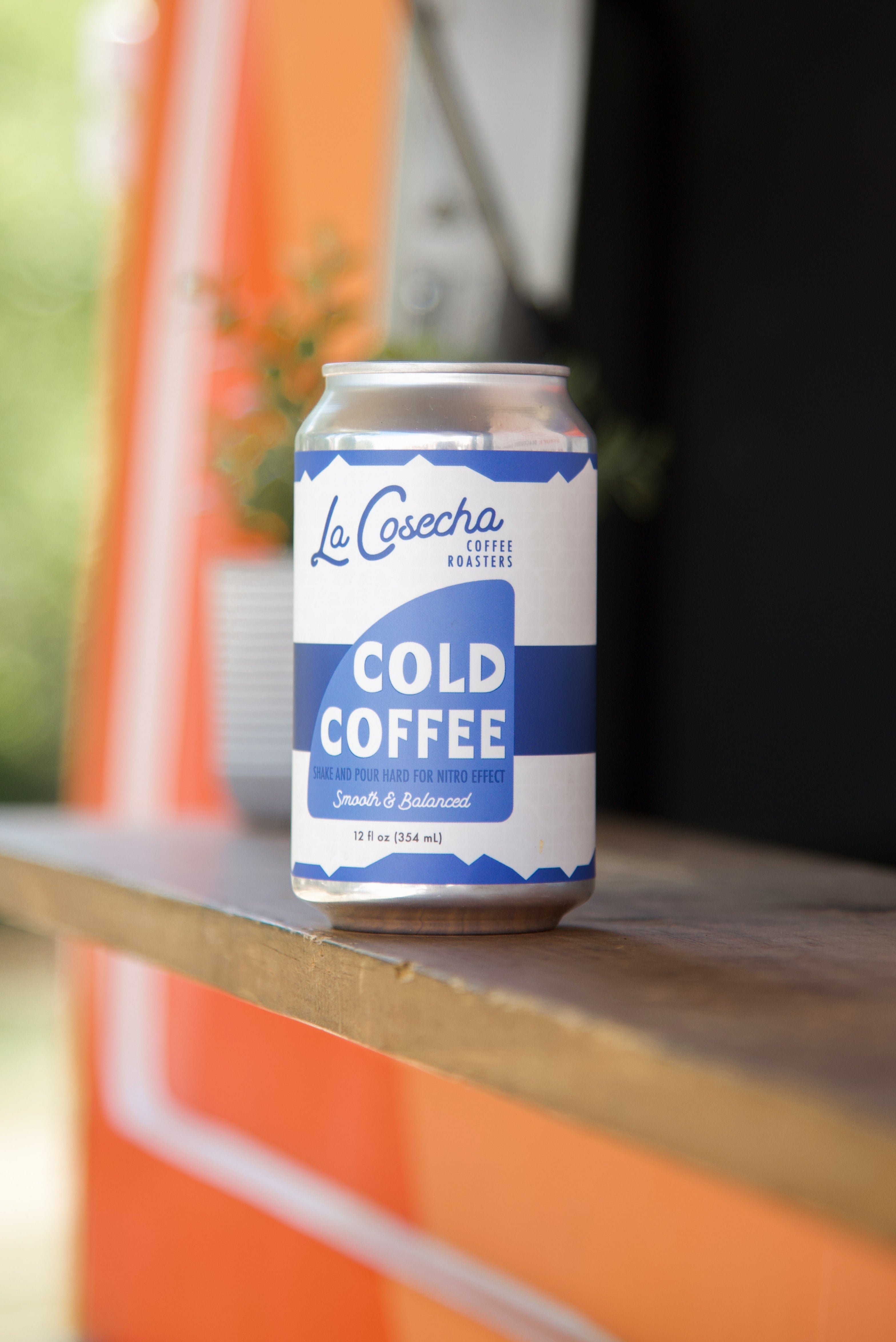 Can of La Cosecha Cold Coffee on a wooden surface with an orange and white background