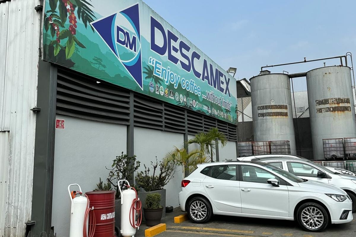 Descamex factory exterior with cars parked in front and a clear sky.