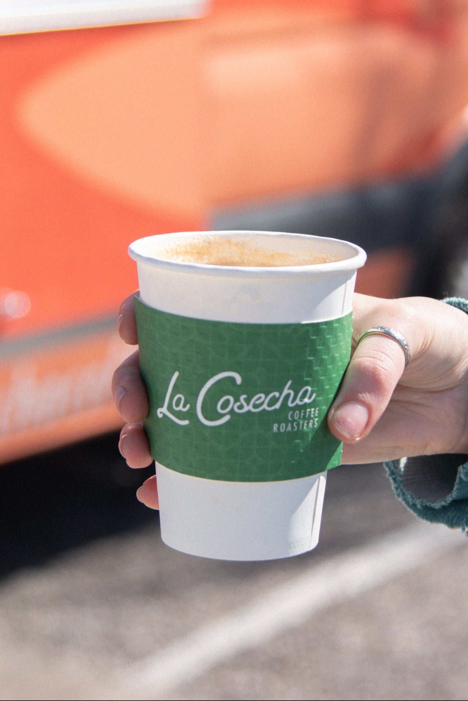 Person holding a coffee cup in front of a La Cosecha branded van.