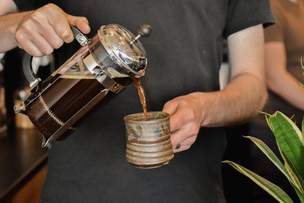Person pouring coffee from a French press into a ceramic cup.