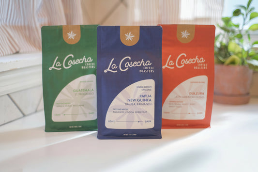 Three La Cosecha coffee packages on a table with a blurred background