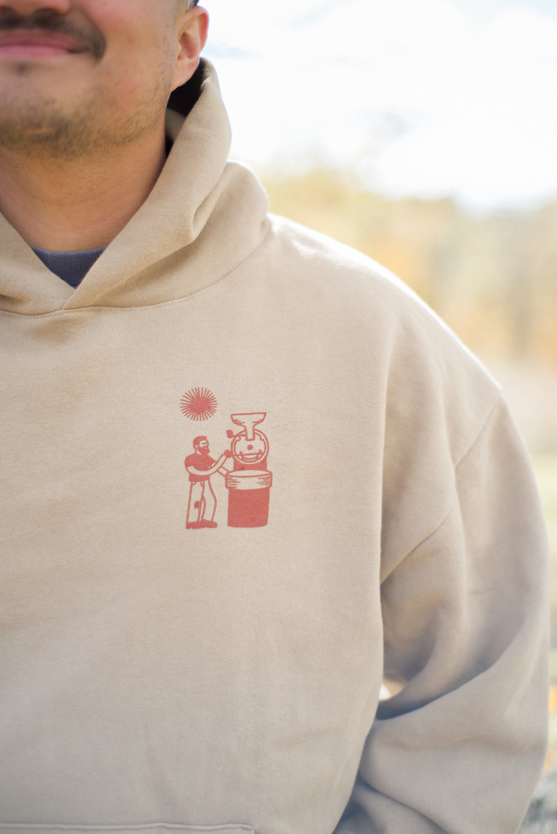 Beige hoodie with a red graphic design on a blurred natural background