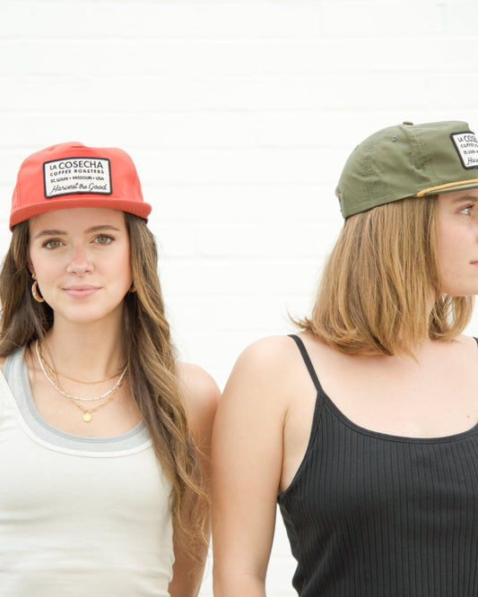 Two women wearing caps with visible branding against a plain background