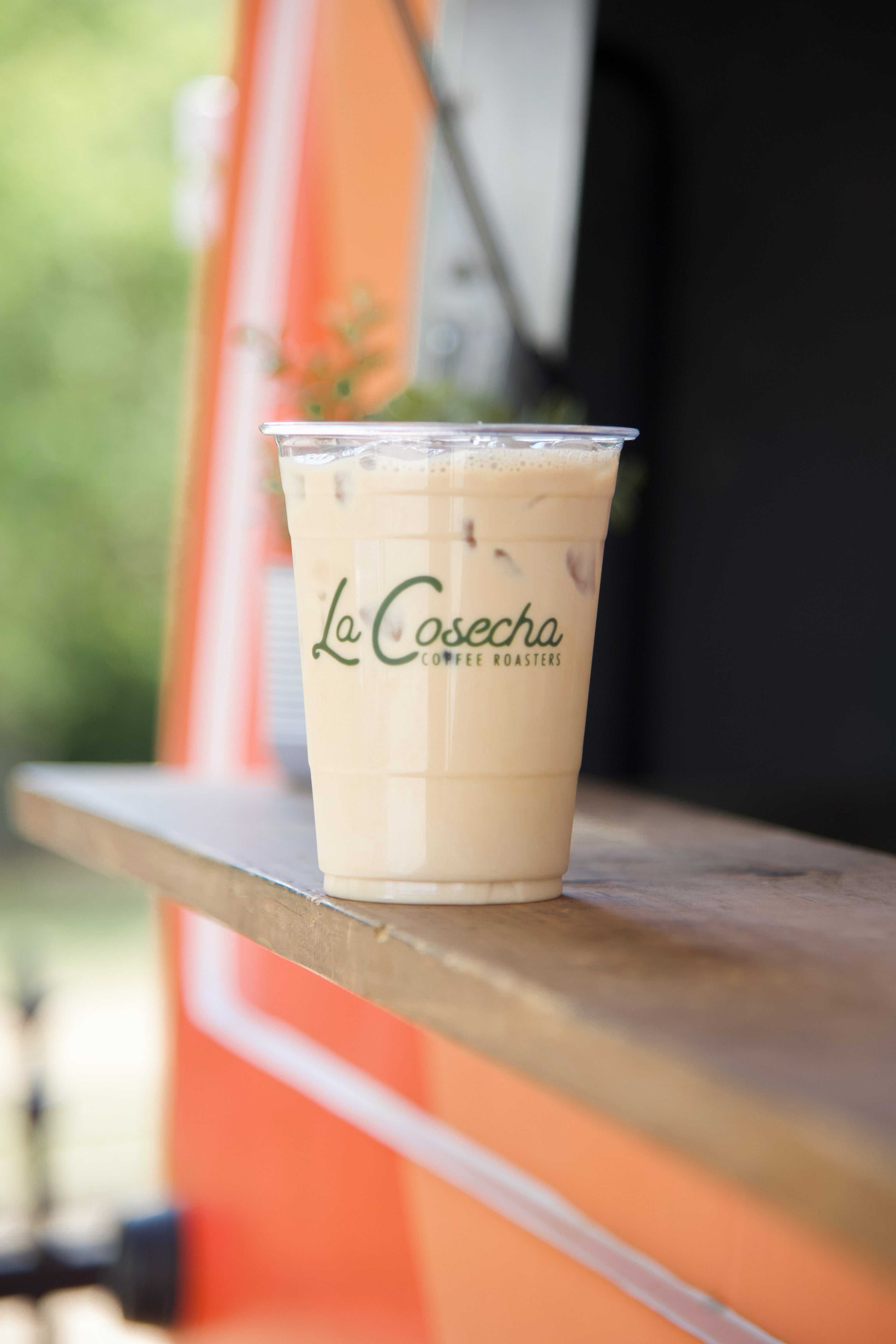 Iced latte with La Cosecha Coffee branding on wooden surface.