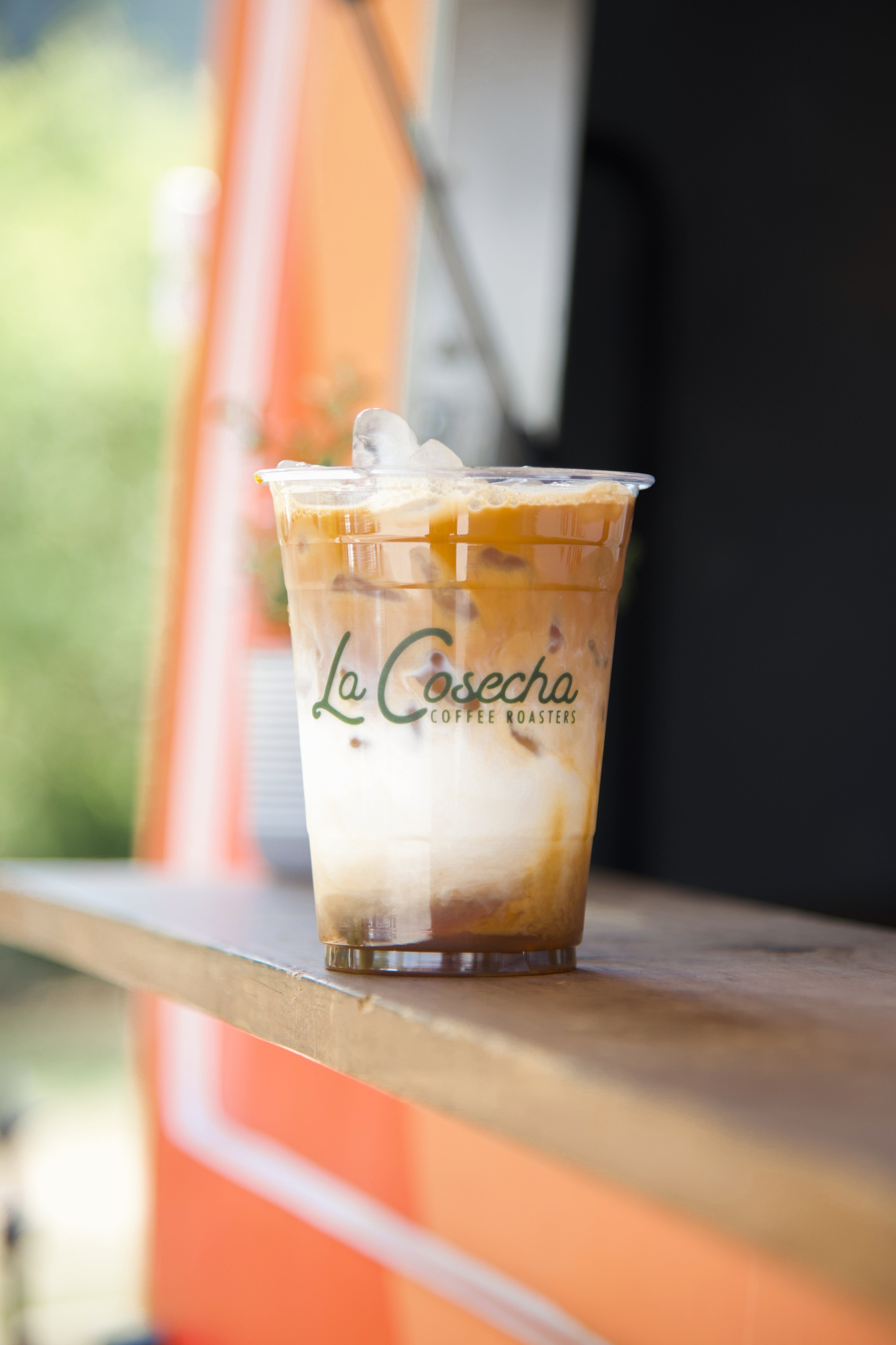Iced coffee in a clear cup with 'La Cosecha' branding on a wooden surface.