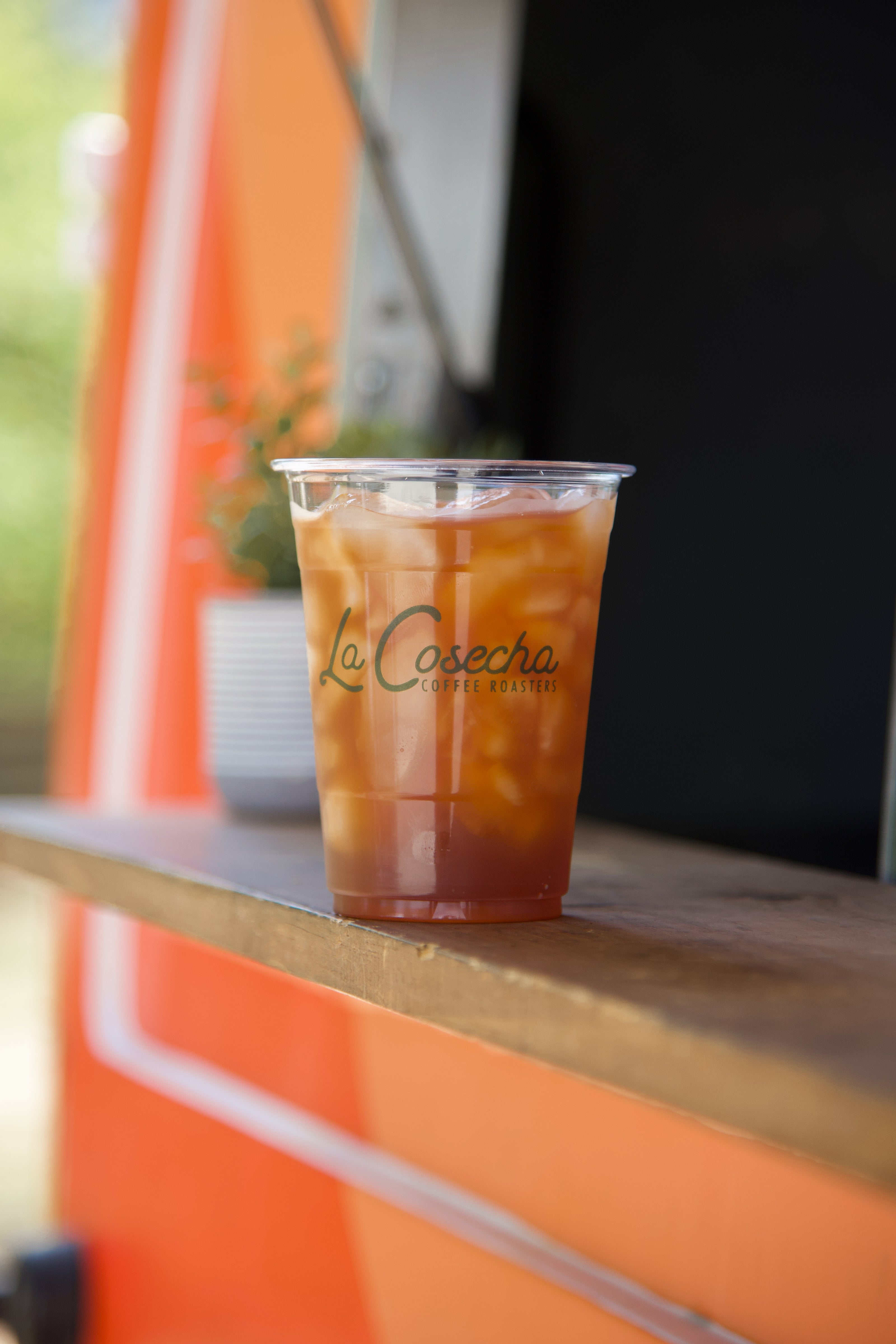 Iced tea in a clear cup with 'La Cosecha' branding on a wooden surface.