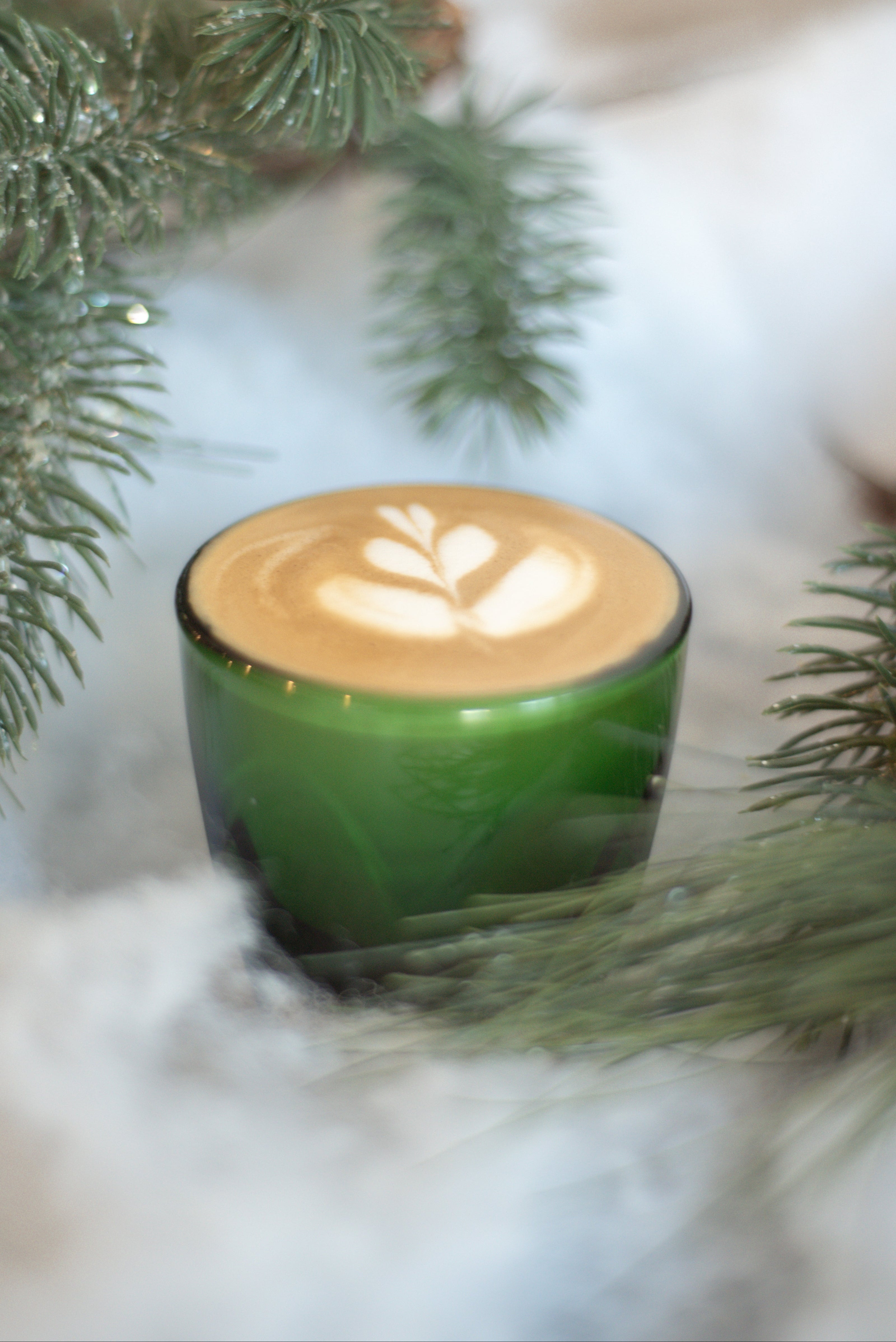 Green mug with a hot beverage surrounded by pine branches and snow