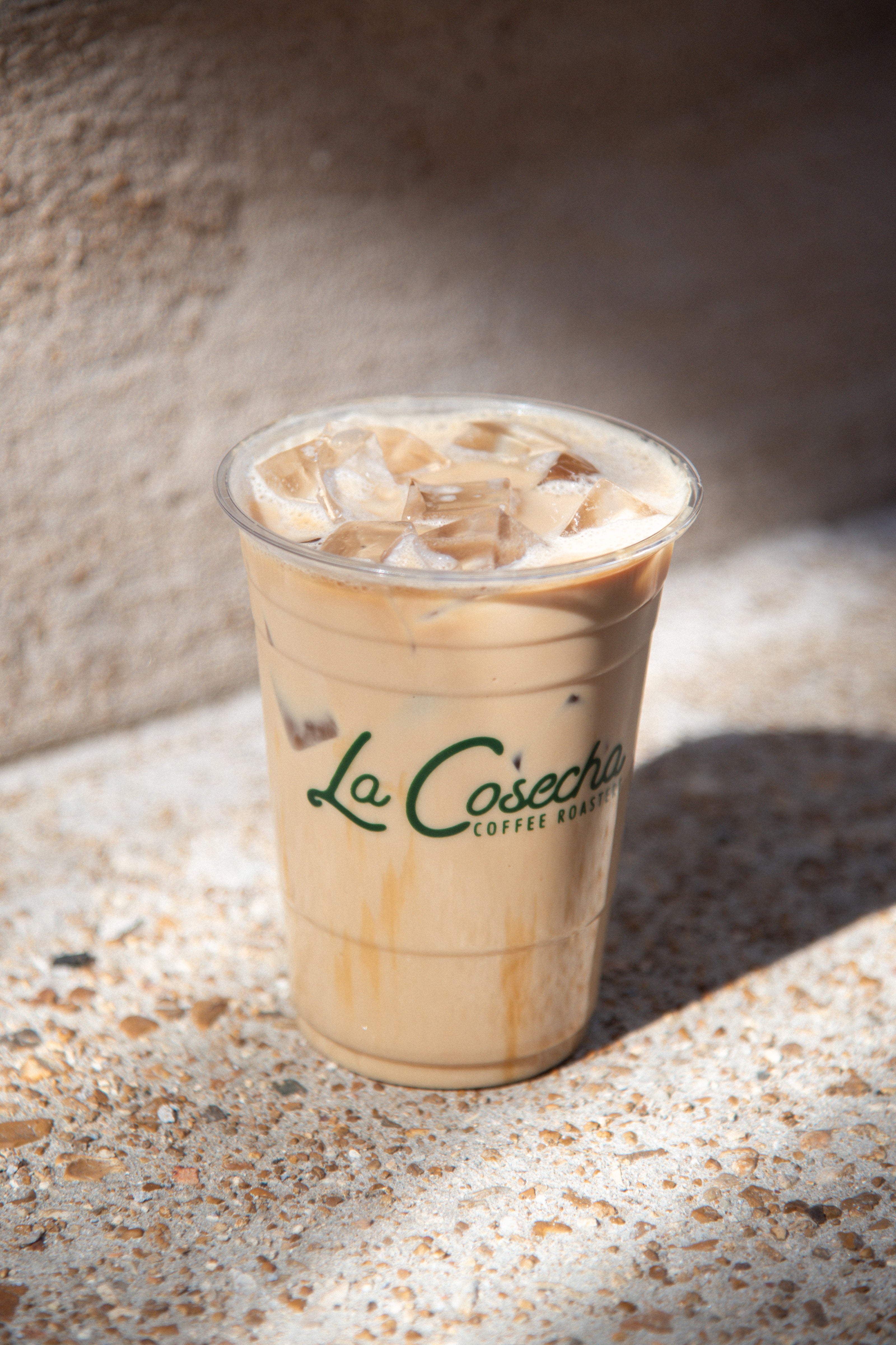 Iced coffee in a clear plastic cup with La Cosecha Coffee Roasters branding on a textured surface.