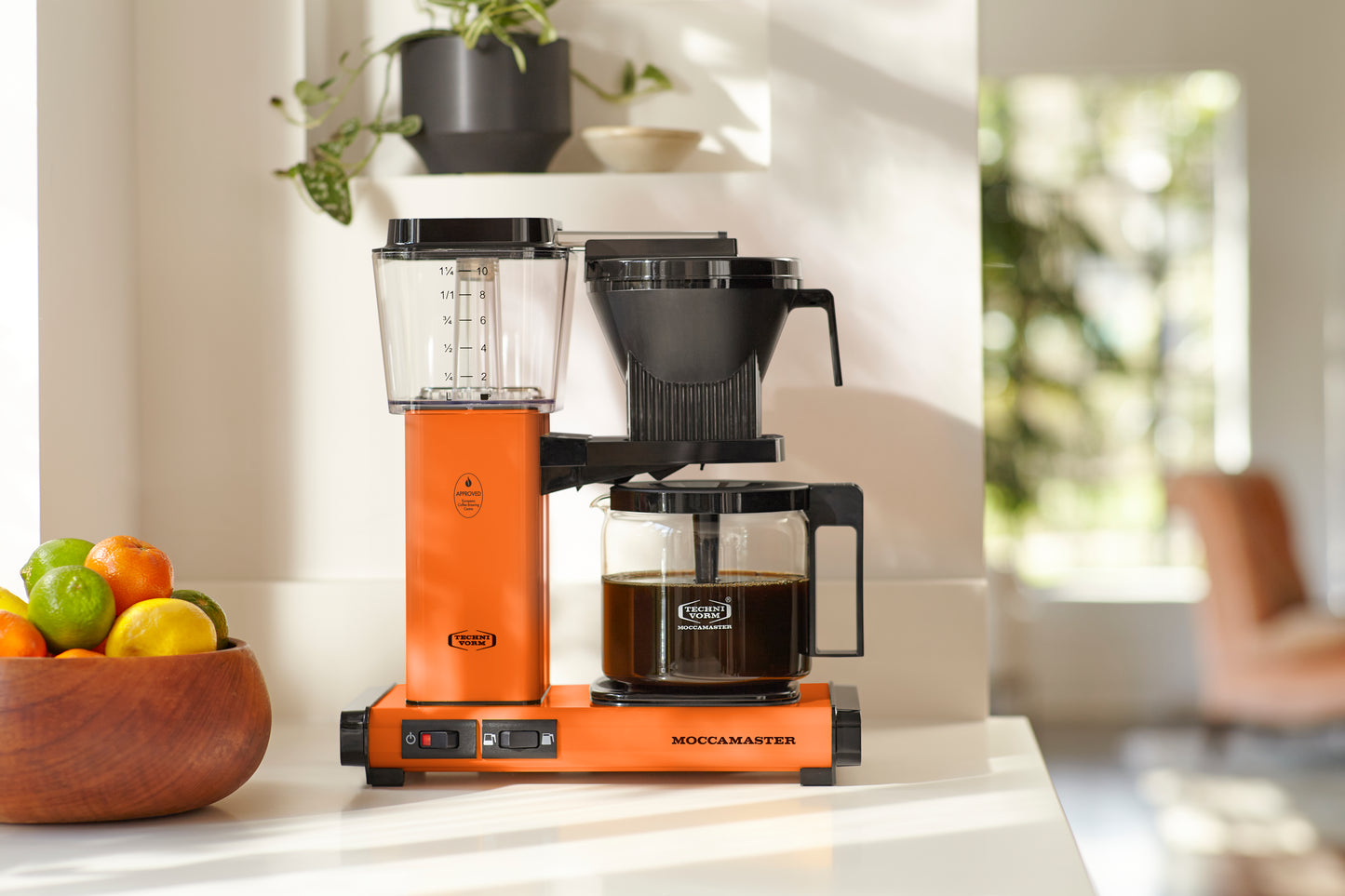 Orange Moccamaster coffee maker on a kitchen counter with a blurred background
