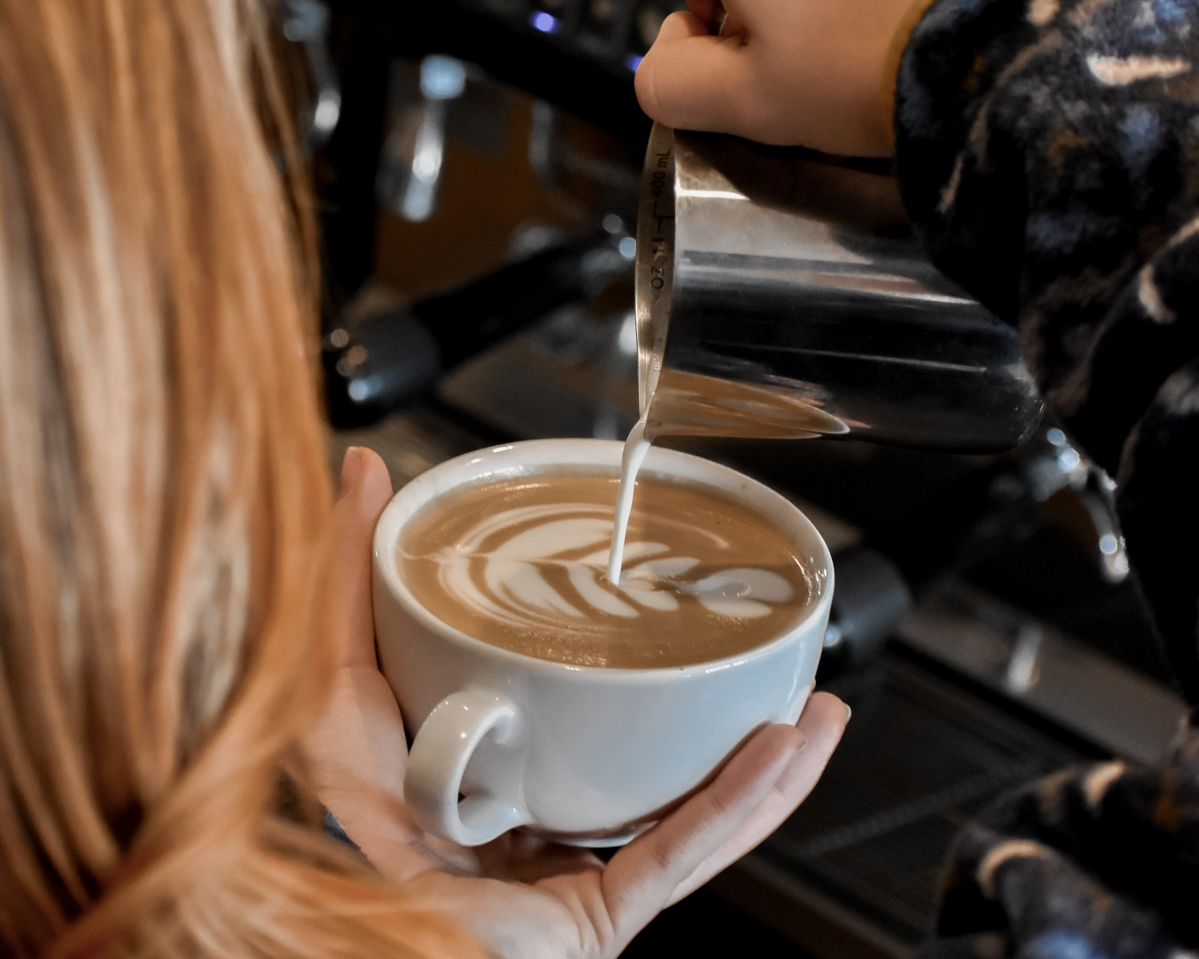 Person pouring steamed milk into a cup of coffee with latte art.