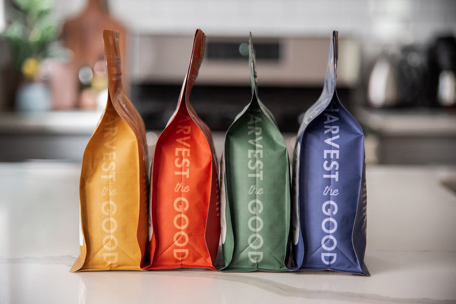 Four 'Harvest the Good' branded packages in different colors on a kitchen counter.