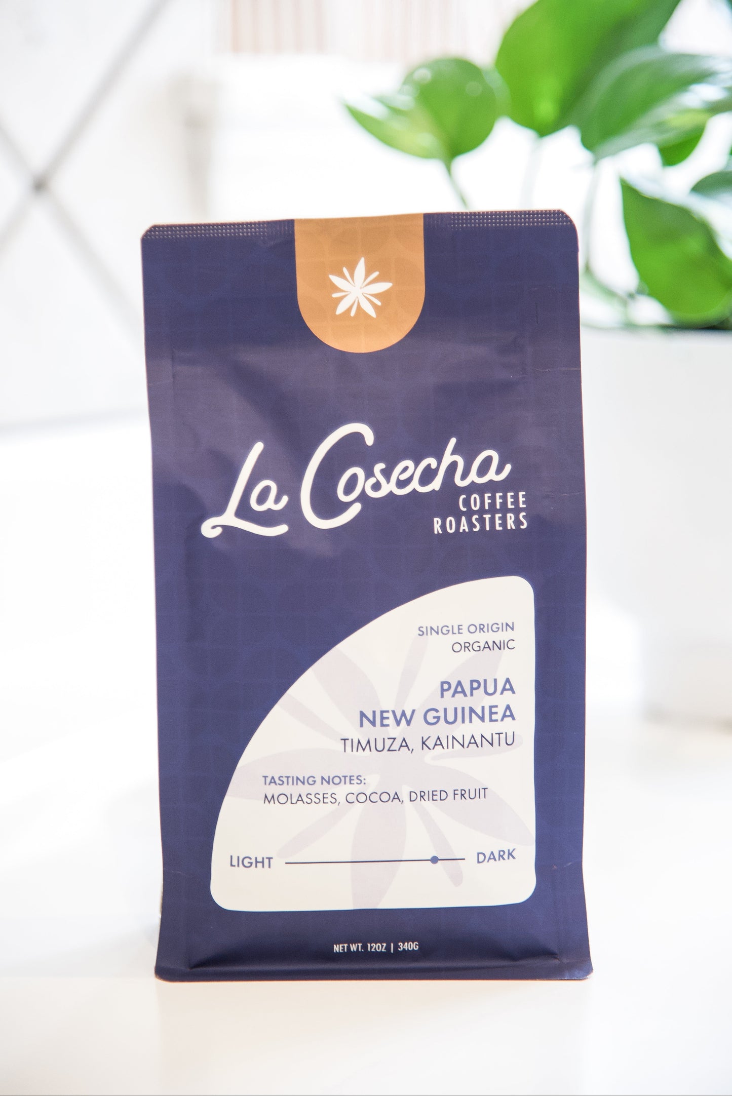 La Cosecha Coffee Roasters bag on a white surface with a blurred plant in the background