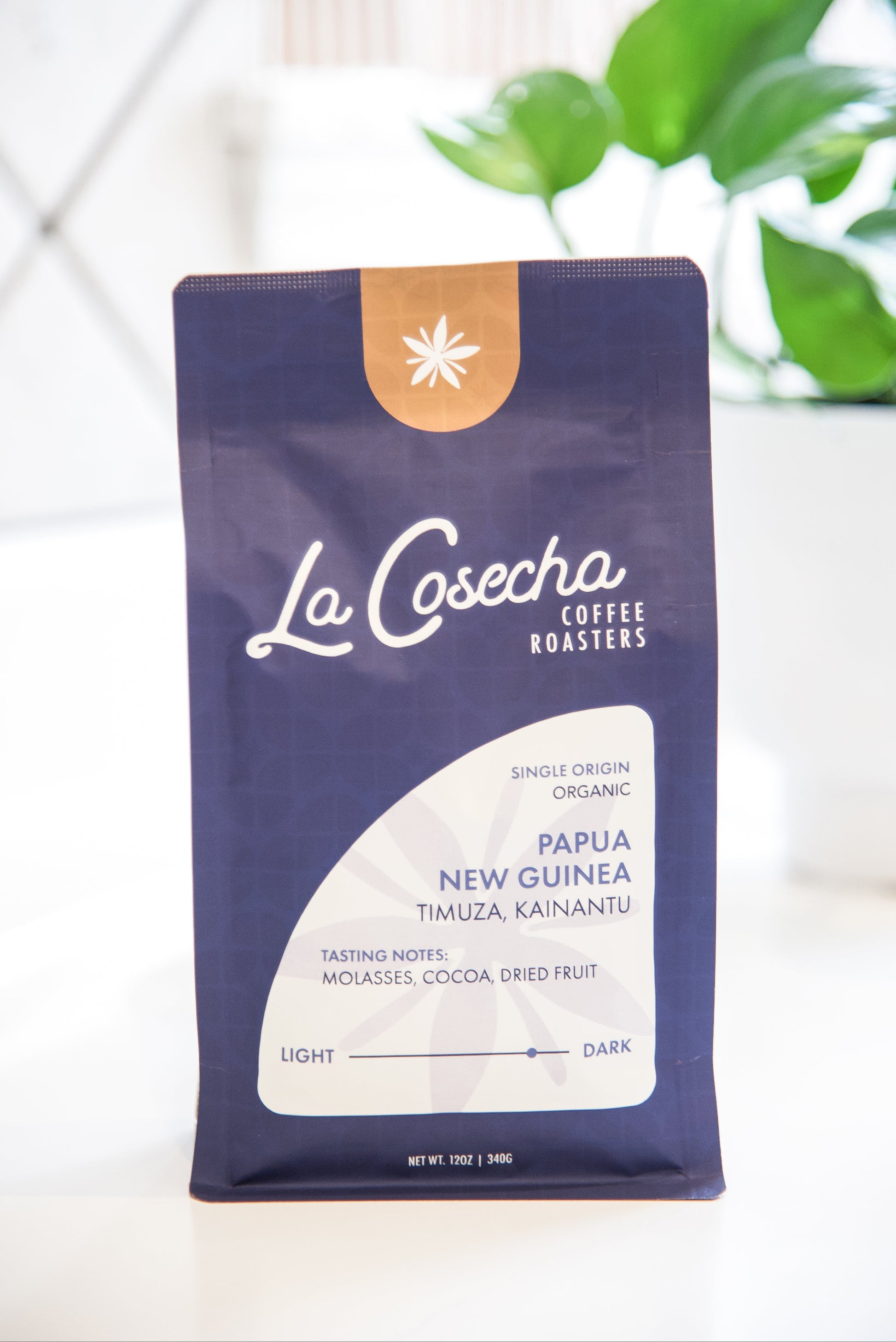 La Cosecha Coffee Roasters bag on a white surface with a blurred plant in the background
