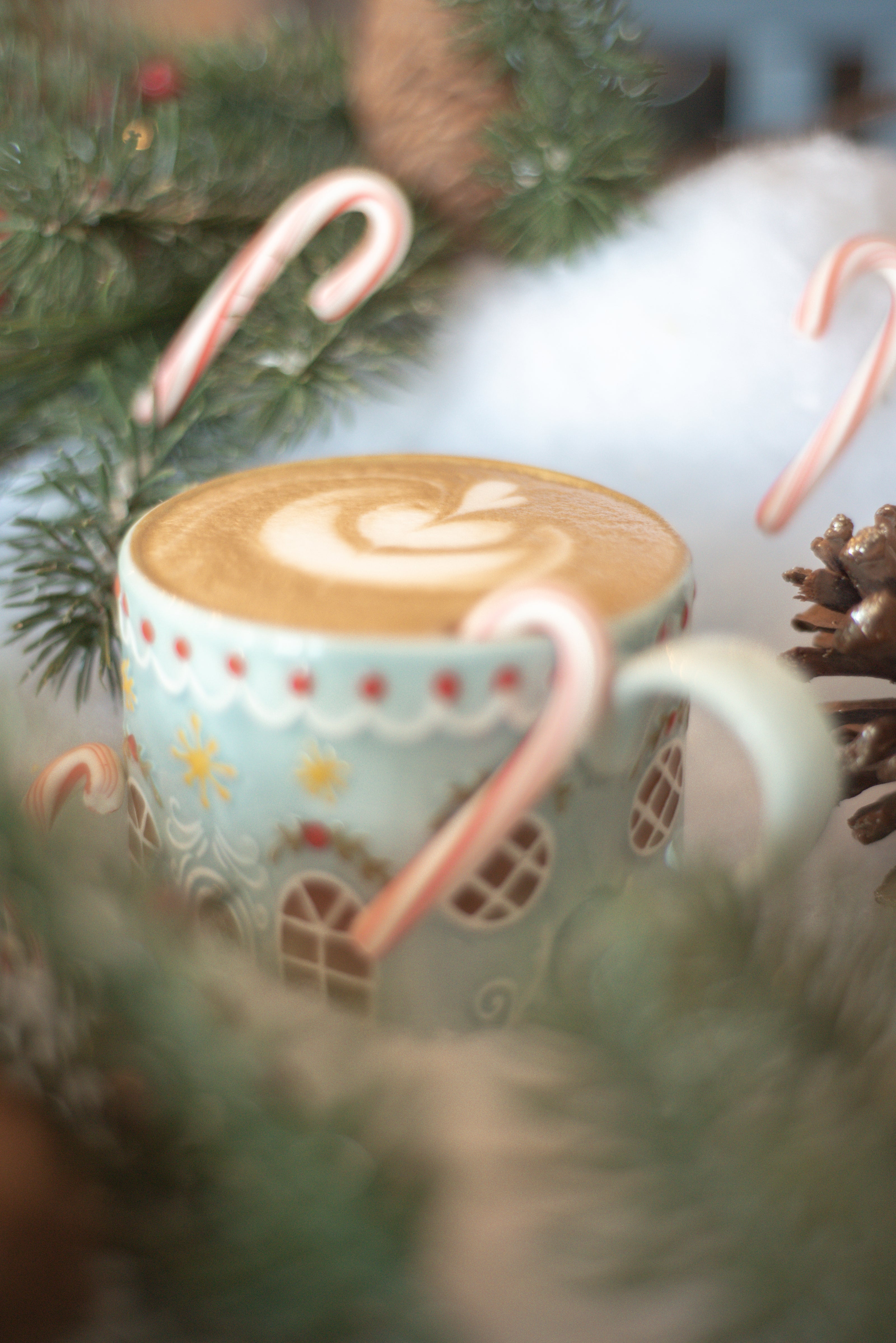 Cup of coffee with candy cane in a decorative mug surrounded by Christmas decorations.