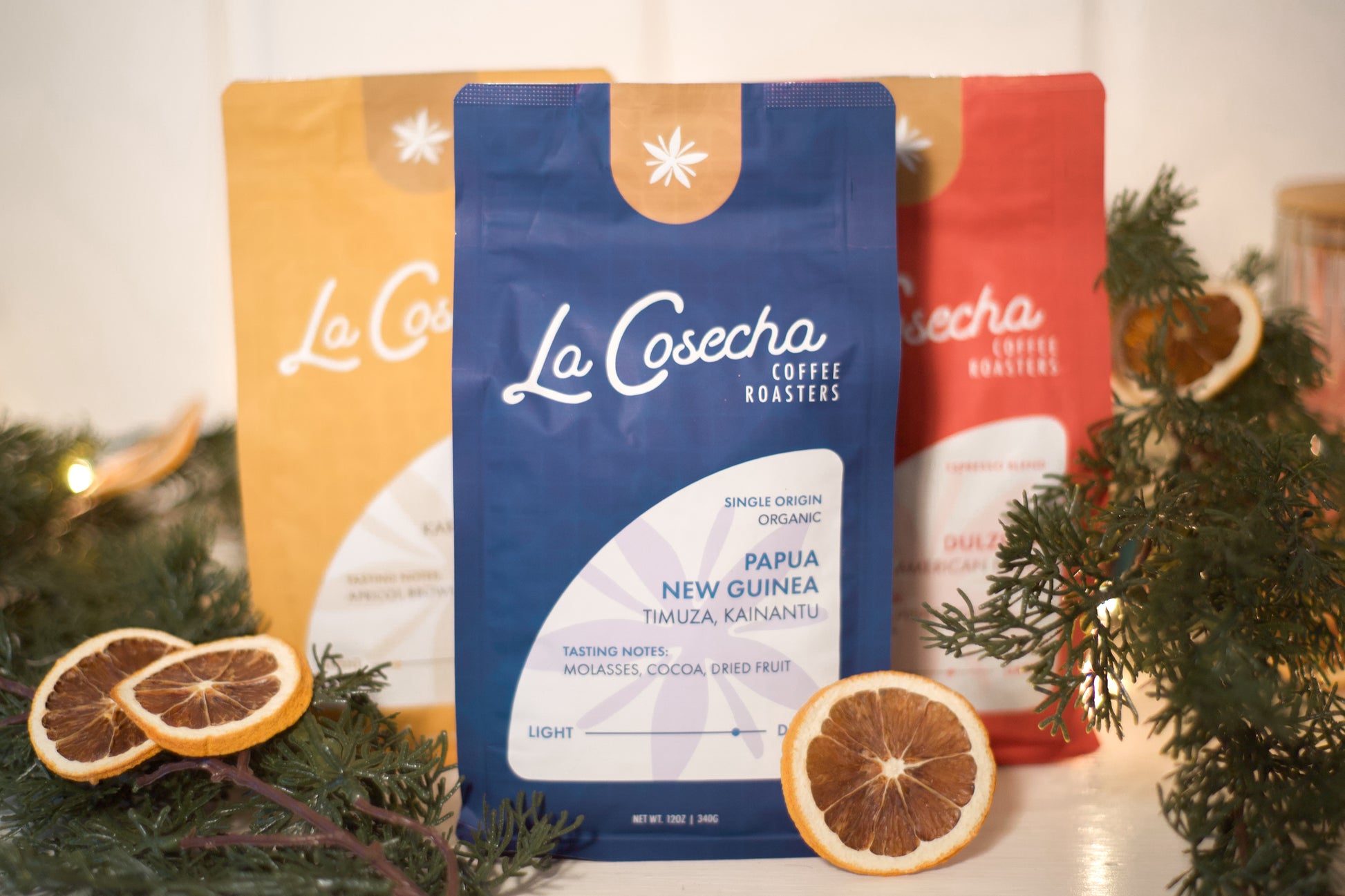 La Cosecha coffee roasters packages with decorative oranges and greenery on a light background