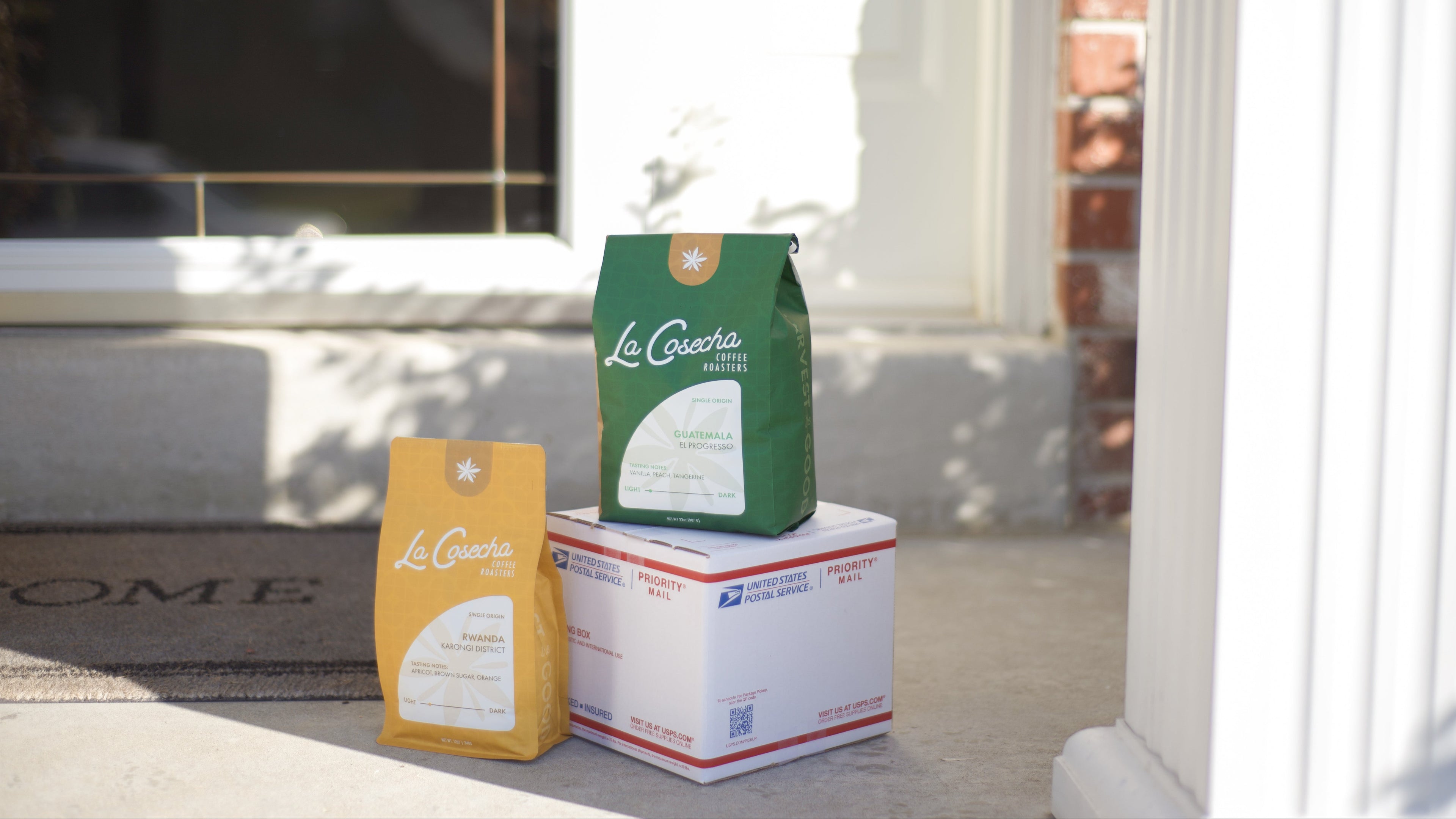 Two coffee bags and a USPS shipping box with La Cosecha Coffee branding. 