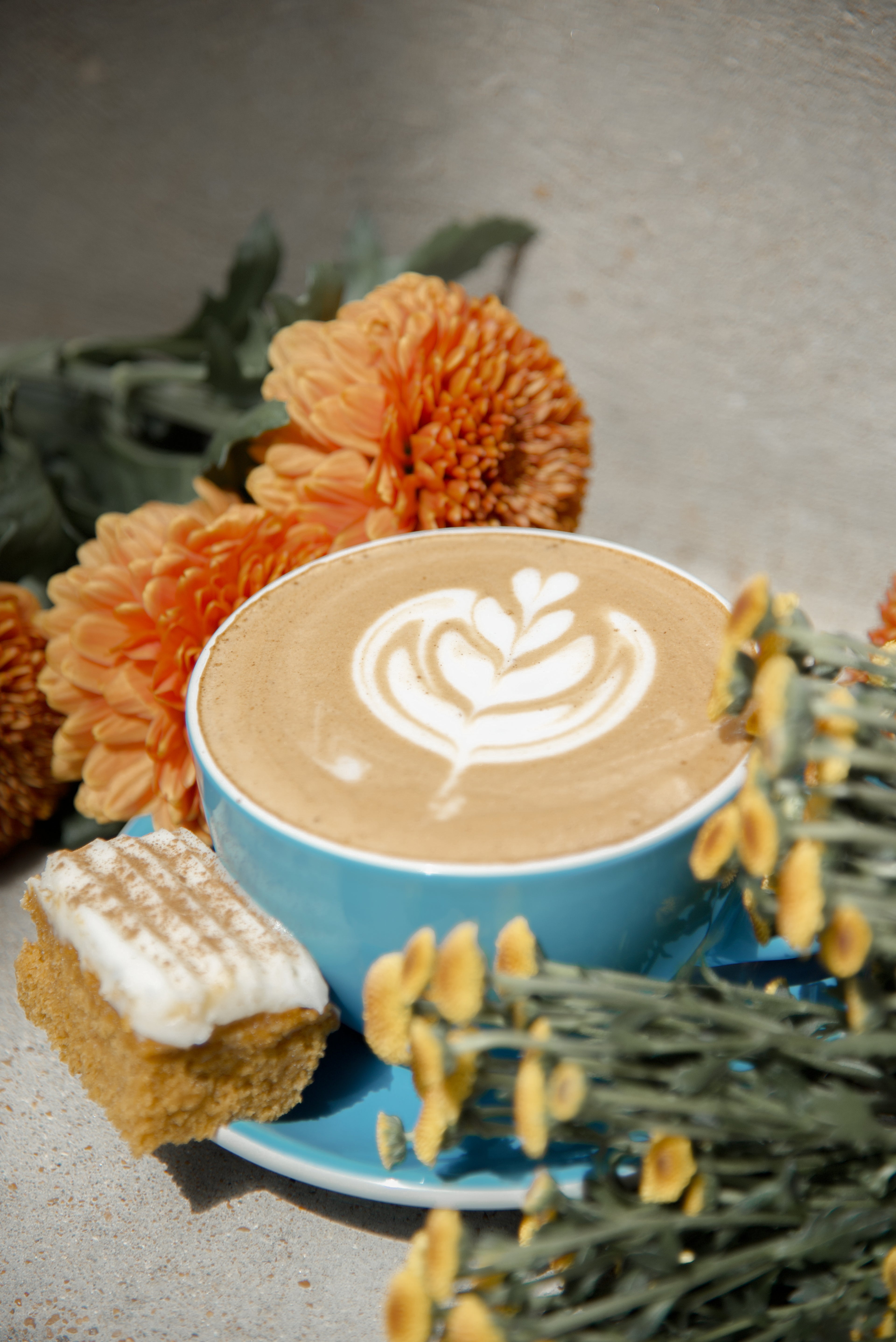Blue cup of coffee with latte art surrounded by flowers on a gray surface