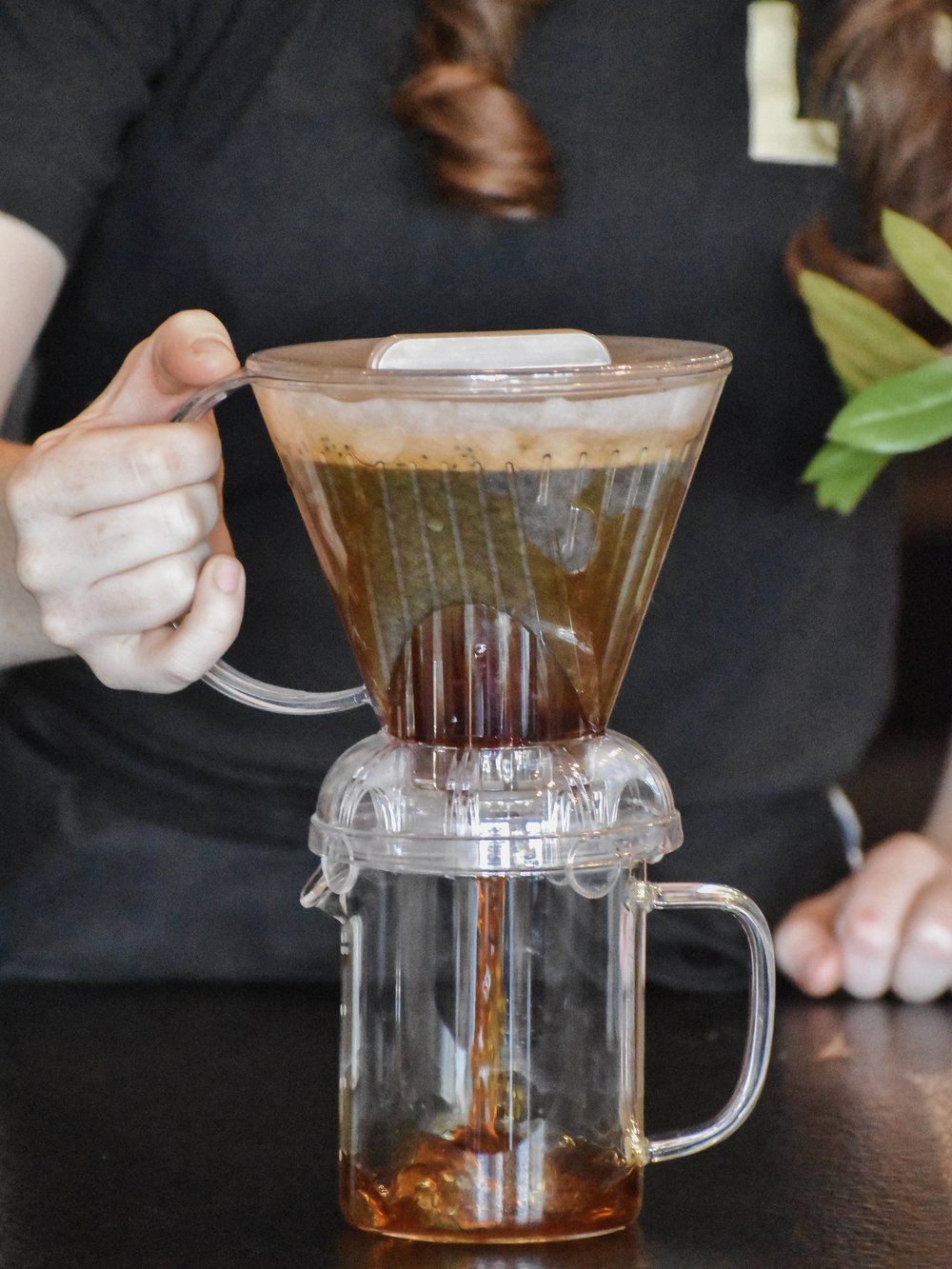 Person holding a glass coffee maker with coffee being brewed.