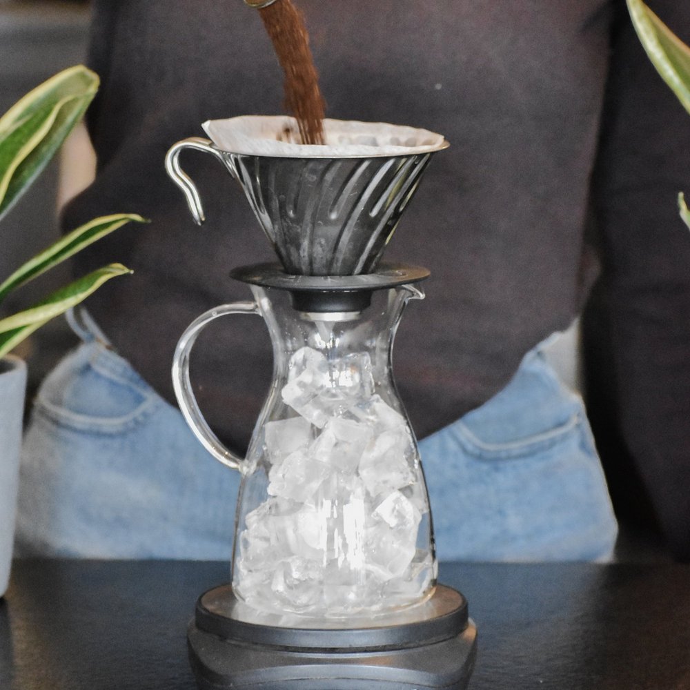 Ice coffee setup with a glass carafe and filter on a table.