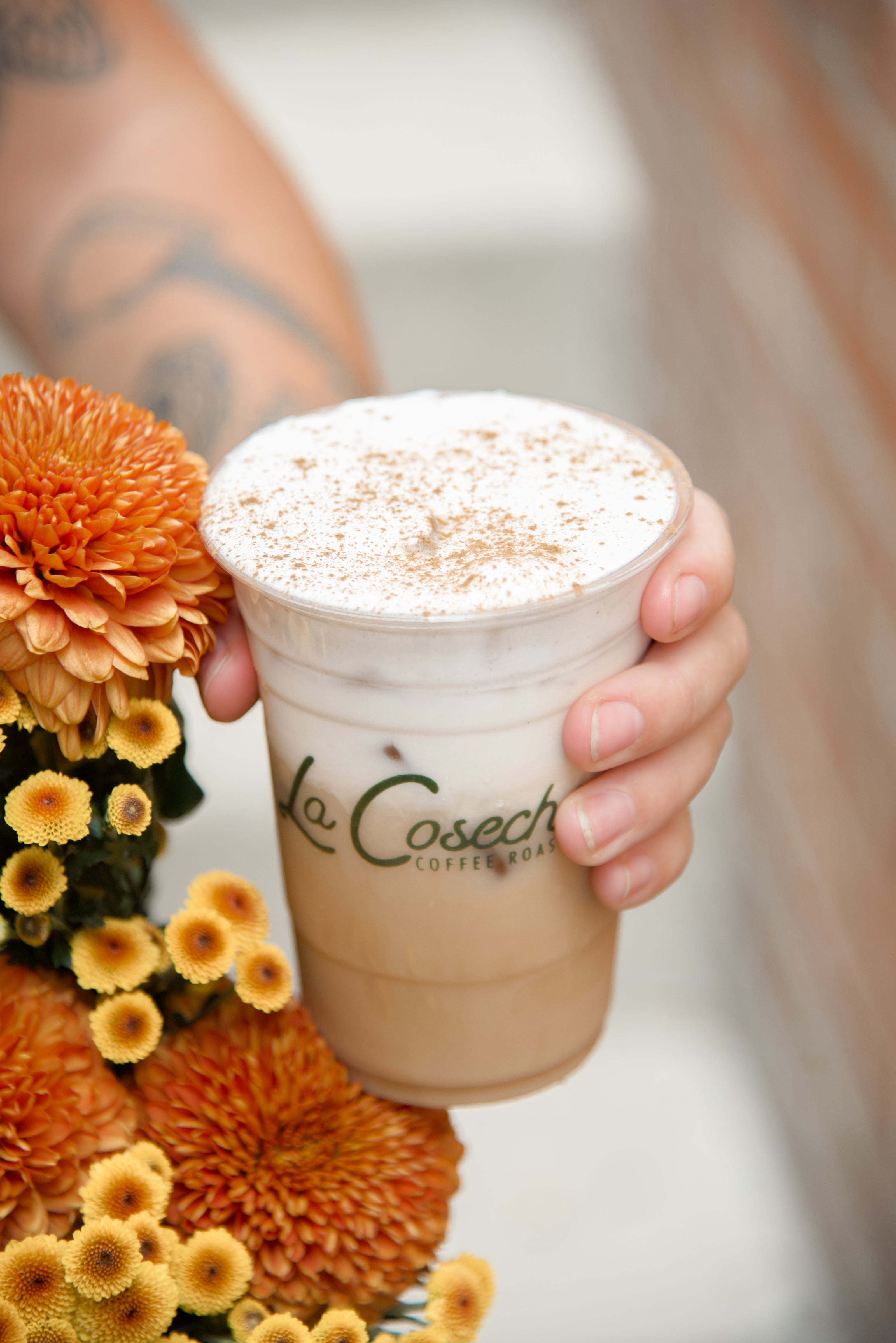 Person holding a La Cosecha coffee cup with flowers in the background
