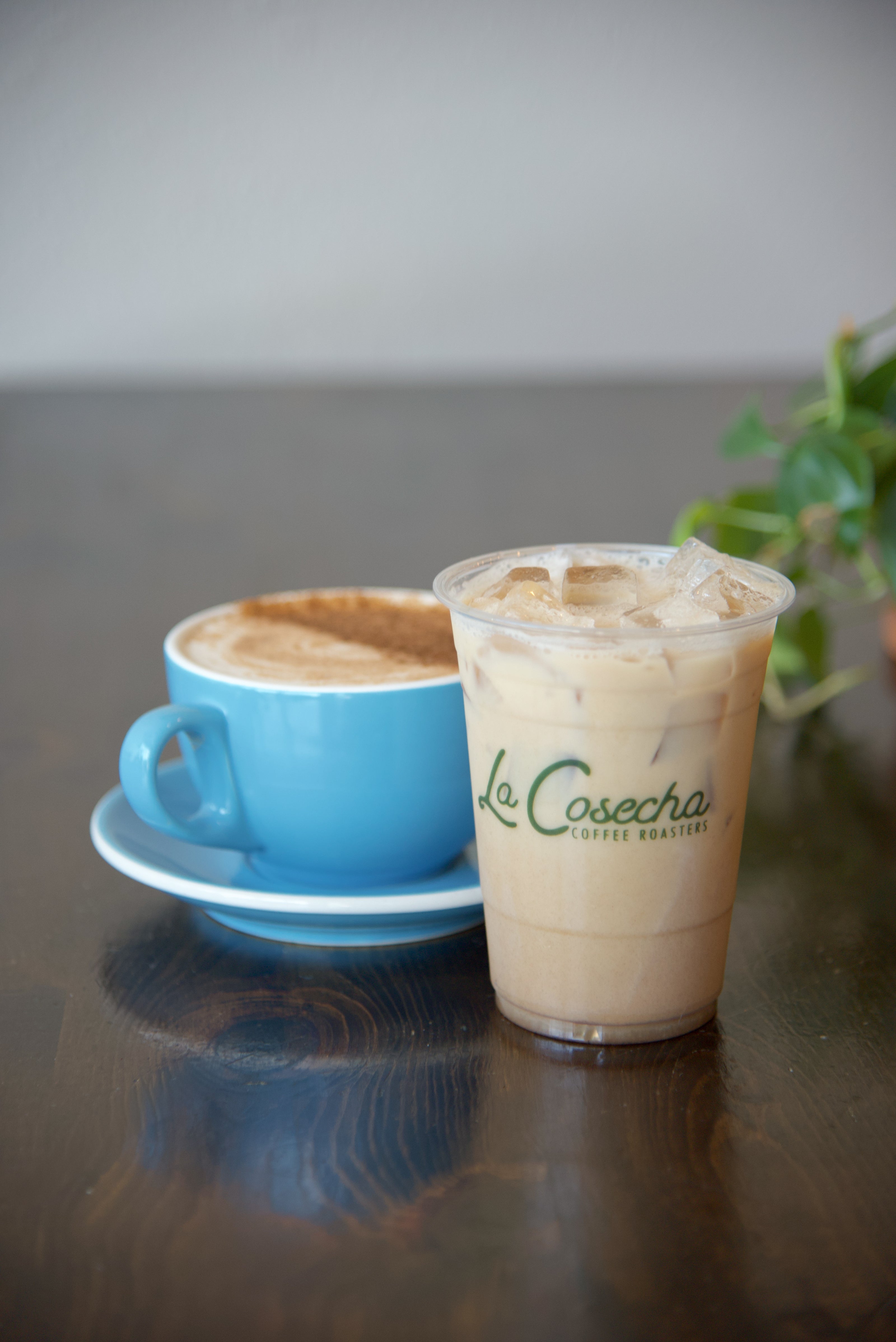 Hot and iced chai latte in blue mug with 'La Cosecha' branding on a wooden table.