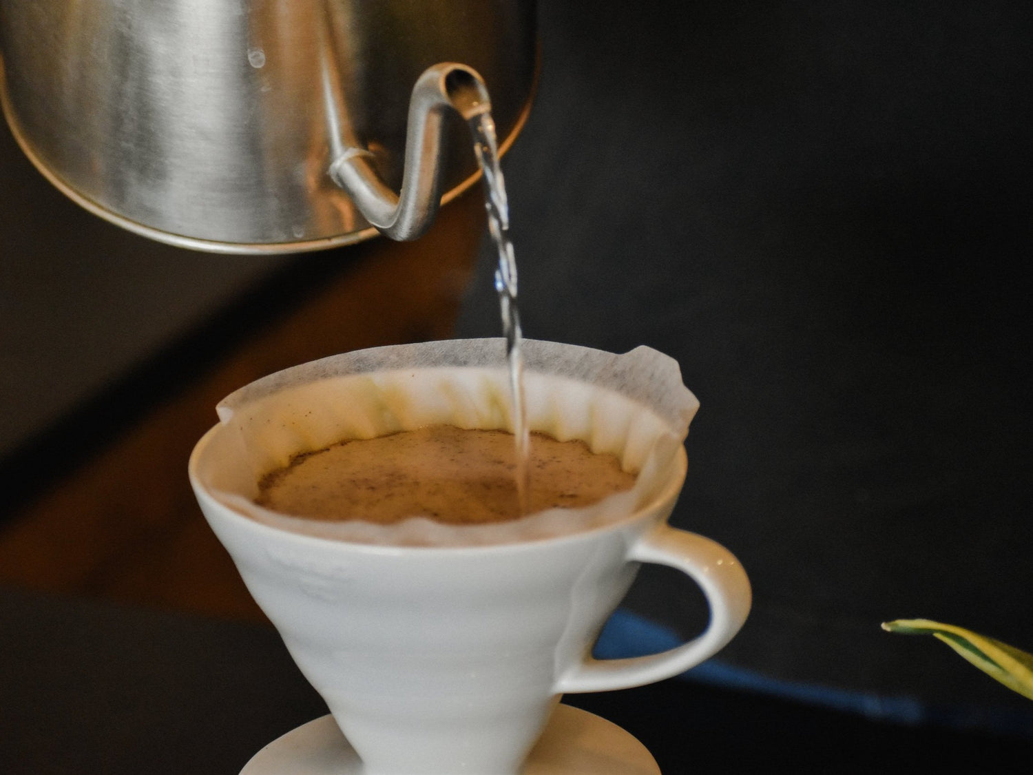 Coffee being poured from a kettle into a white coffee filter on a dark background