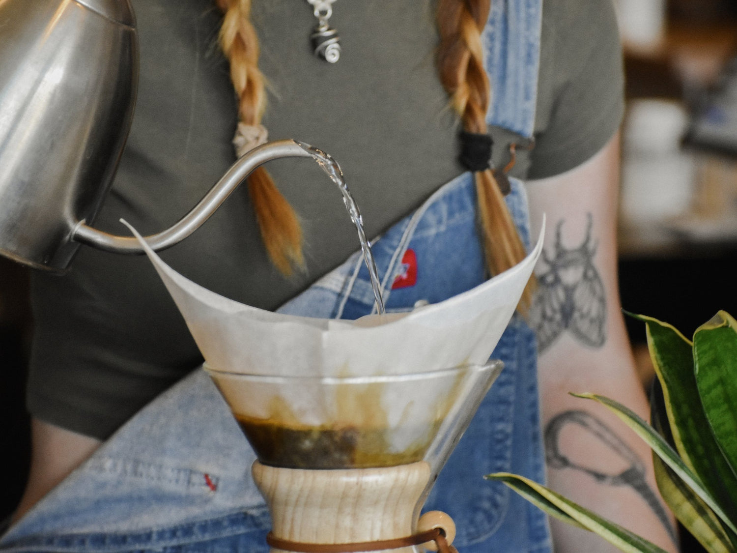Person making coffee using a pour-over method with a metal kettle and paper filter.
