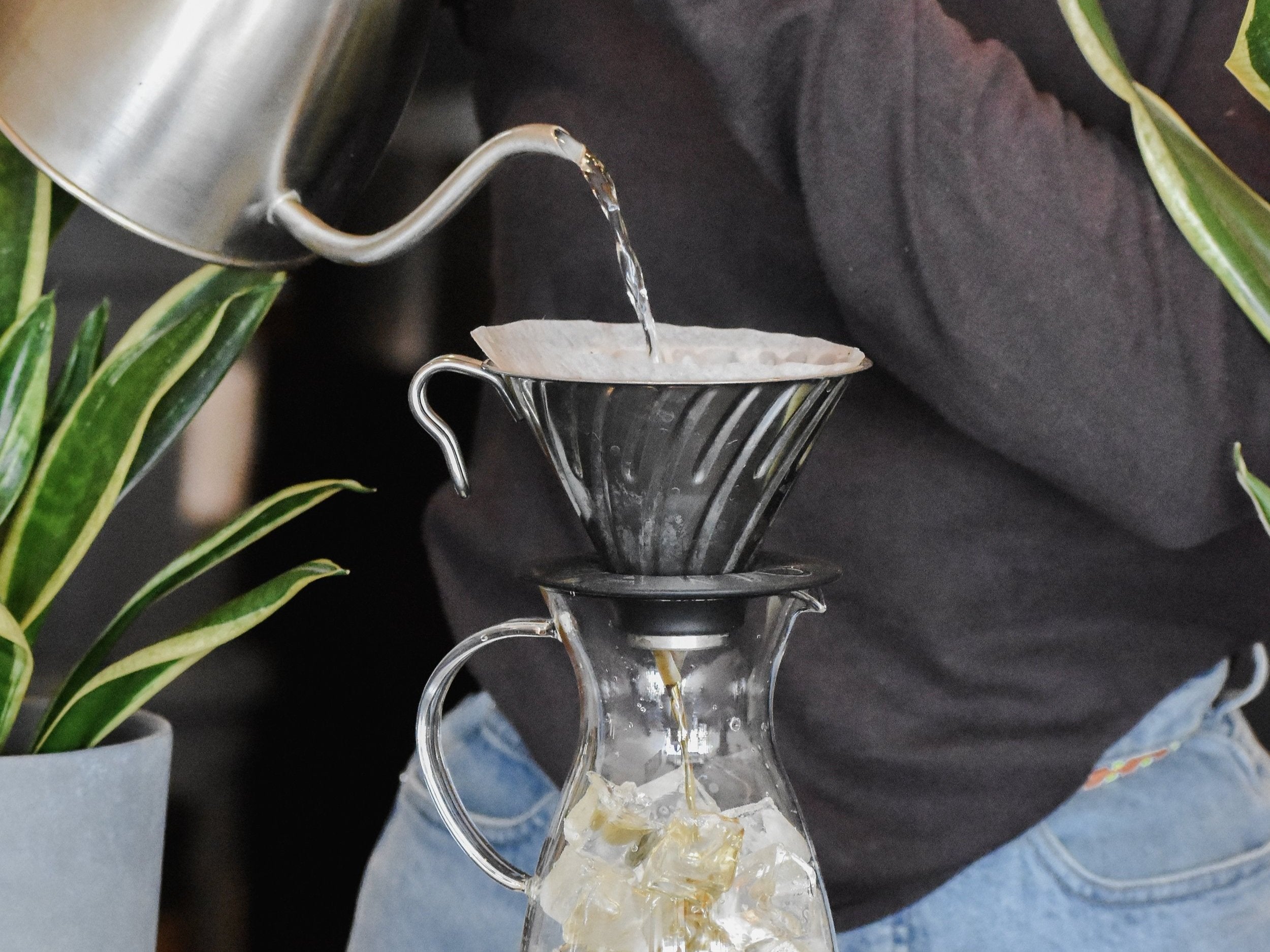 Person pouring water from a kettle into a glass carafe with a coffee filter.