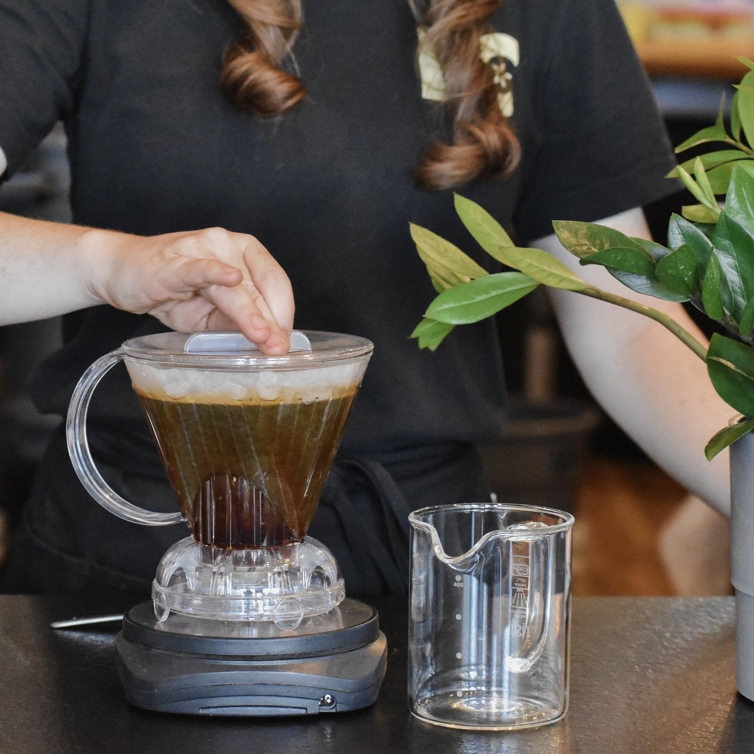 Person making a coffee drink using a clear glass pitcher and a small glass container on a table.