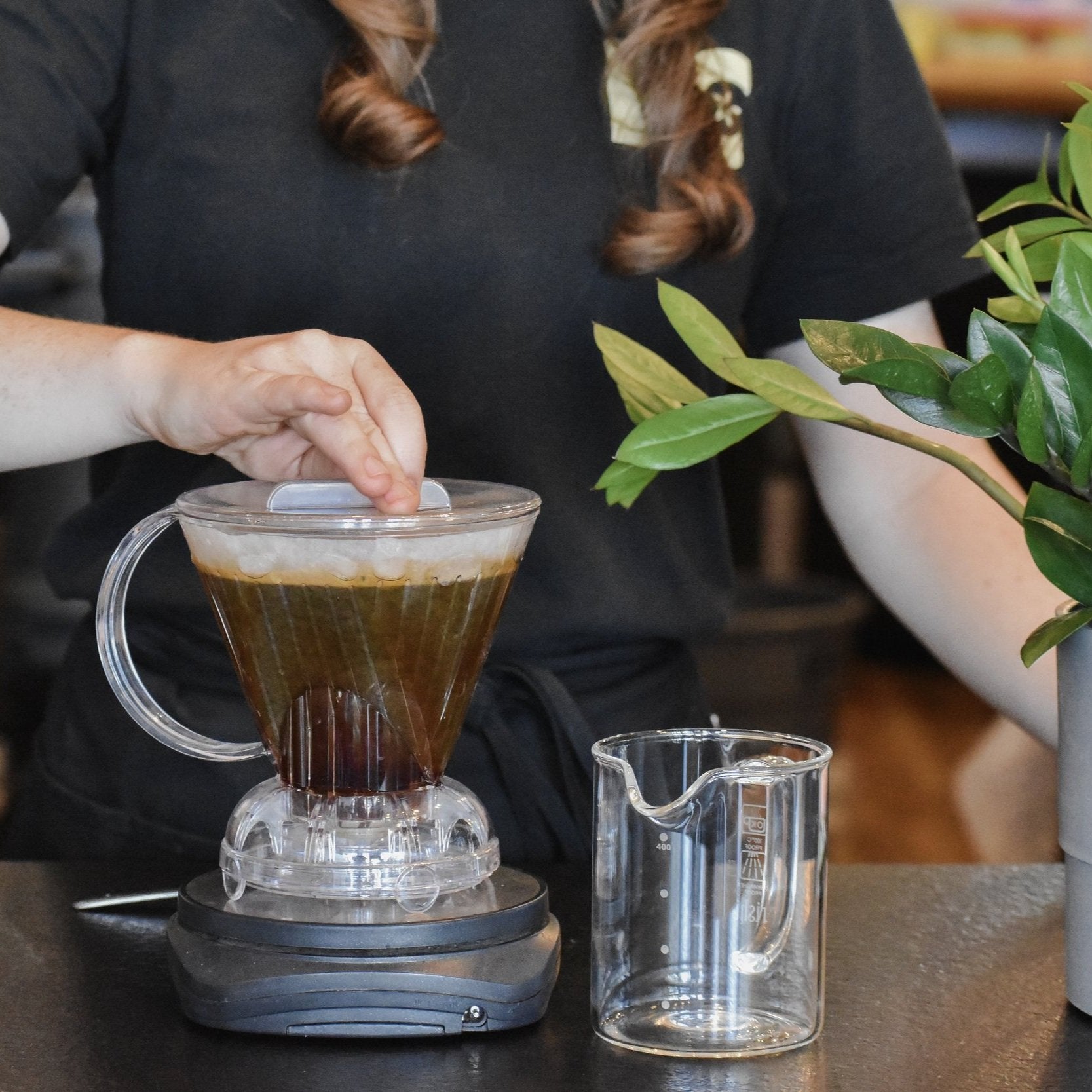 Person making a coffee drink using a clear glass pitcher and a small glass container on a table.