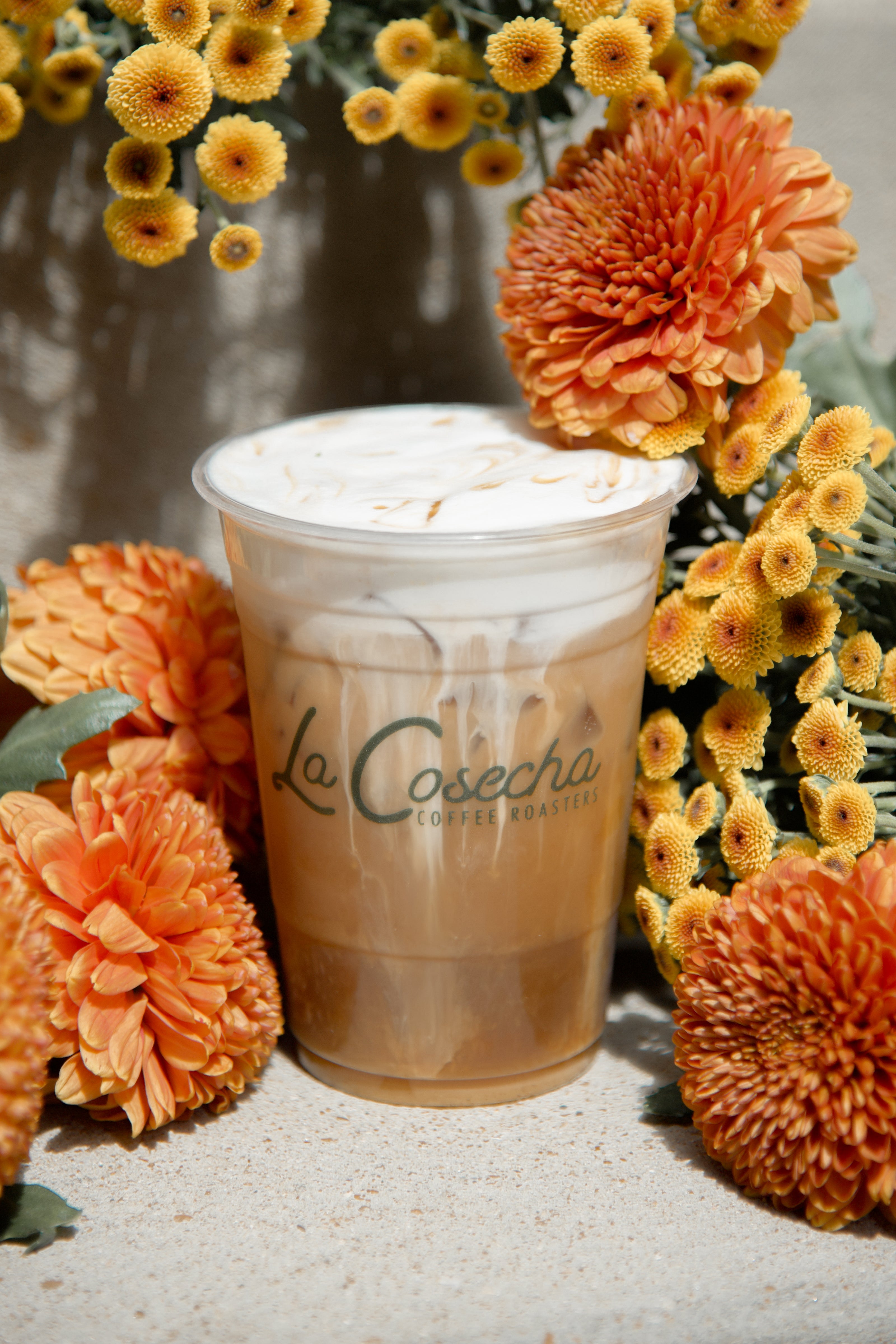 Le Cosecha coffee cup surrounded by orange and yellow flowers on a textured surface